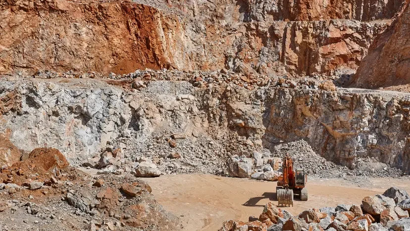 An excavator working in a rocky quarry with steep, layered rock walls.