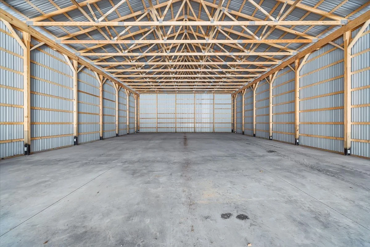 Empty warehouse with concrete floor, metal walls, and wooden roof trusses.