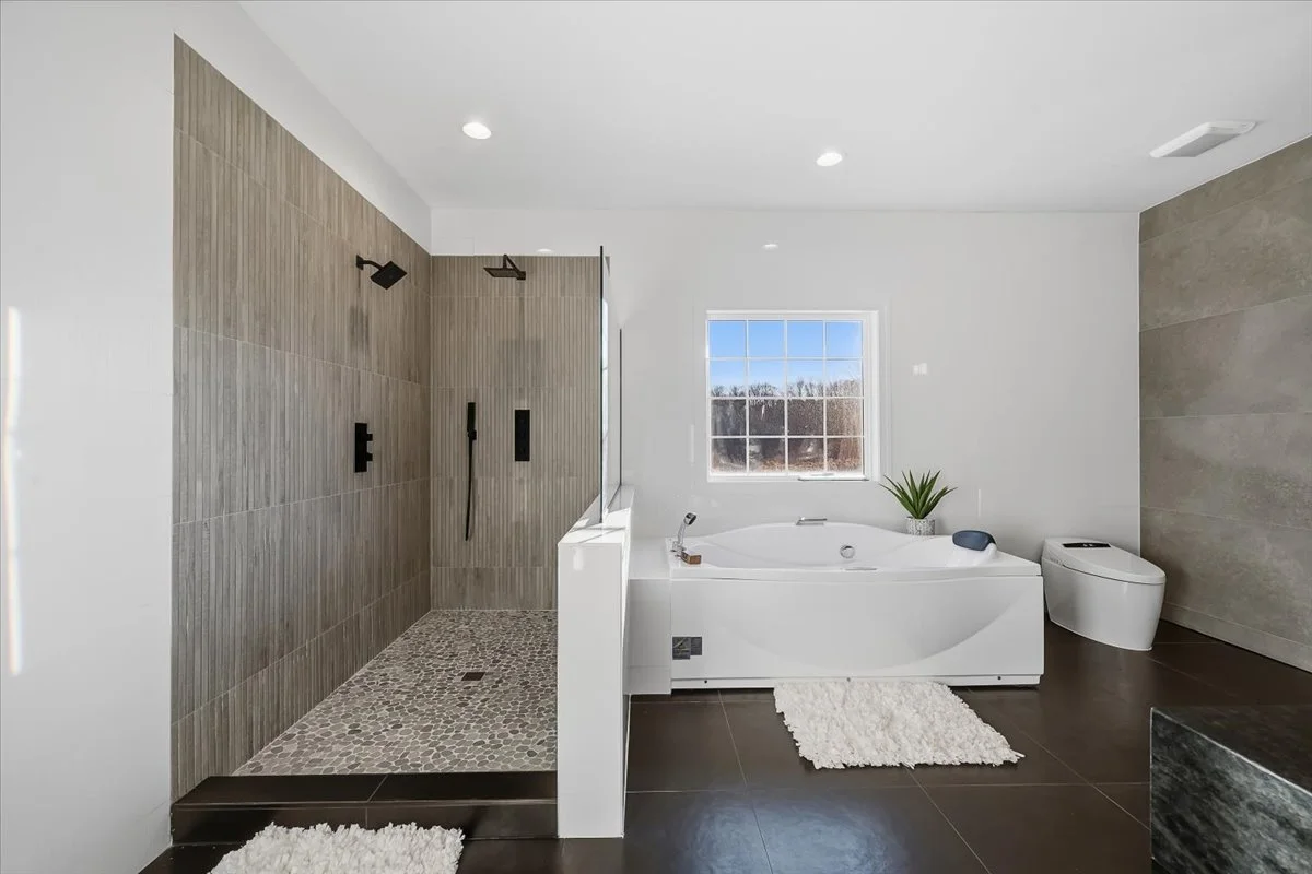 Modern bathroom with a walk-in shower, bathtub, and toilet, featuring neutral colors, a plant, and a window showing an outdoor scene.