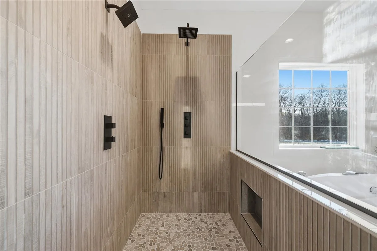 Modern bathroom shower area with wooden wall tiles, black shower fixtures, and a window showing a winter scene outside.