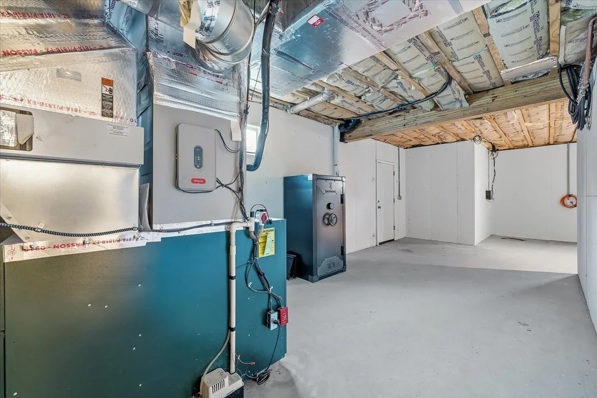 Empty unfinished utility or storage room with exposed insulation and electrical wiring on the ceiling, and some metal equipment and panels on the wall.