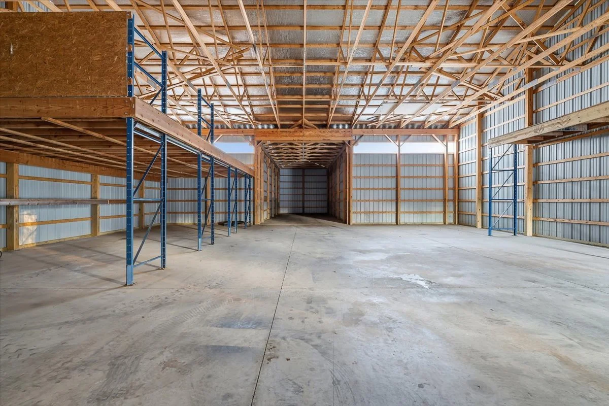 Empty warehouse or garage with unfinished wooden and metal framing, concrete floor, and high ceiling.