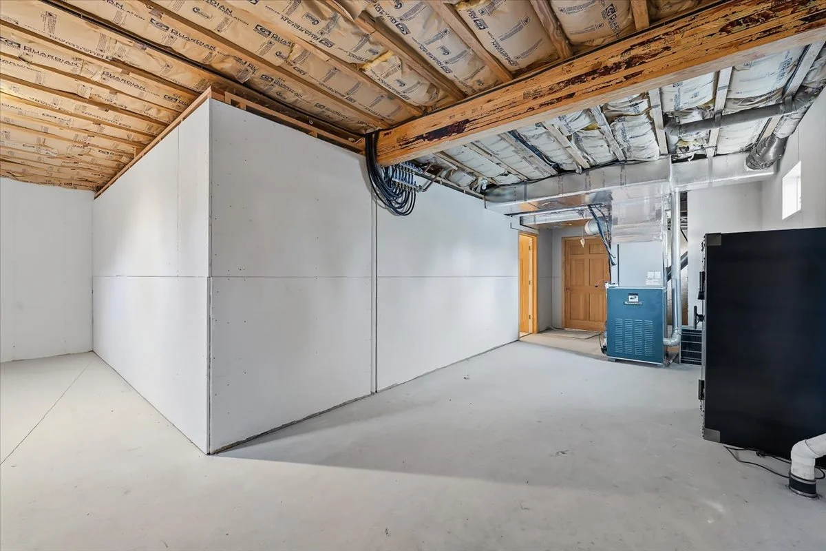 Unfinished basement with drywall partitions, visible insulation, and HVAC equipment.