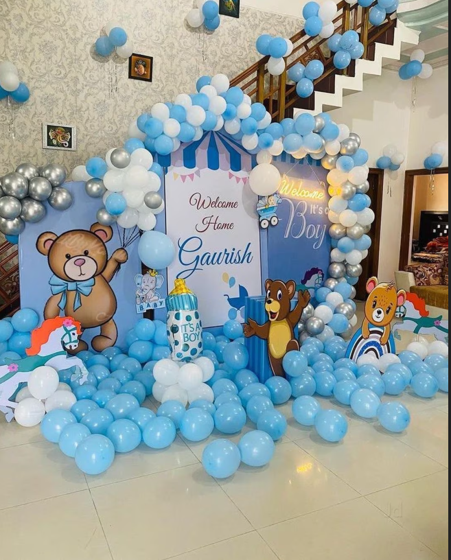 Decorations for a boy's birthday with cartoon animal characters, blue, white, and silver balloons, a cake, and a welcome sign for Gaurish.