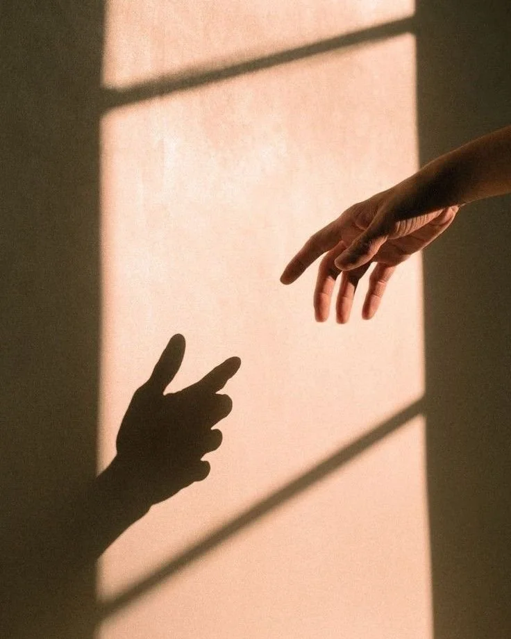 Shadow of a hand with two fingers raised, casting a shadow in the shape of a bunny, on a wall illuminated by sunlight.