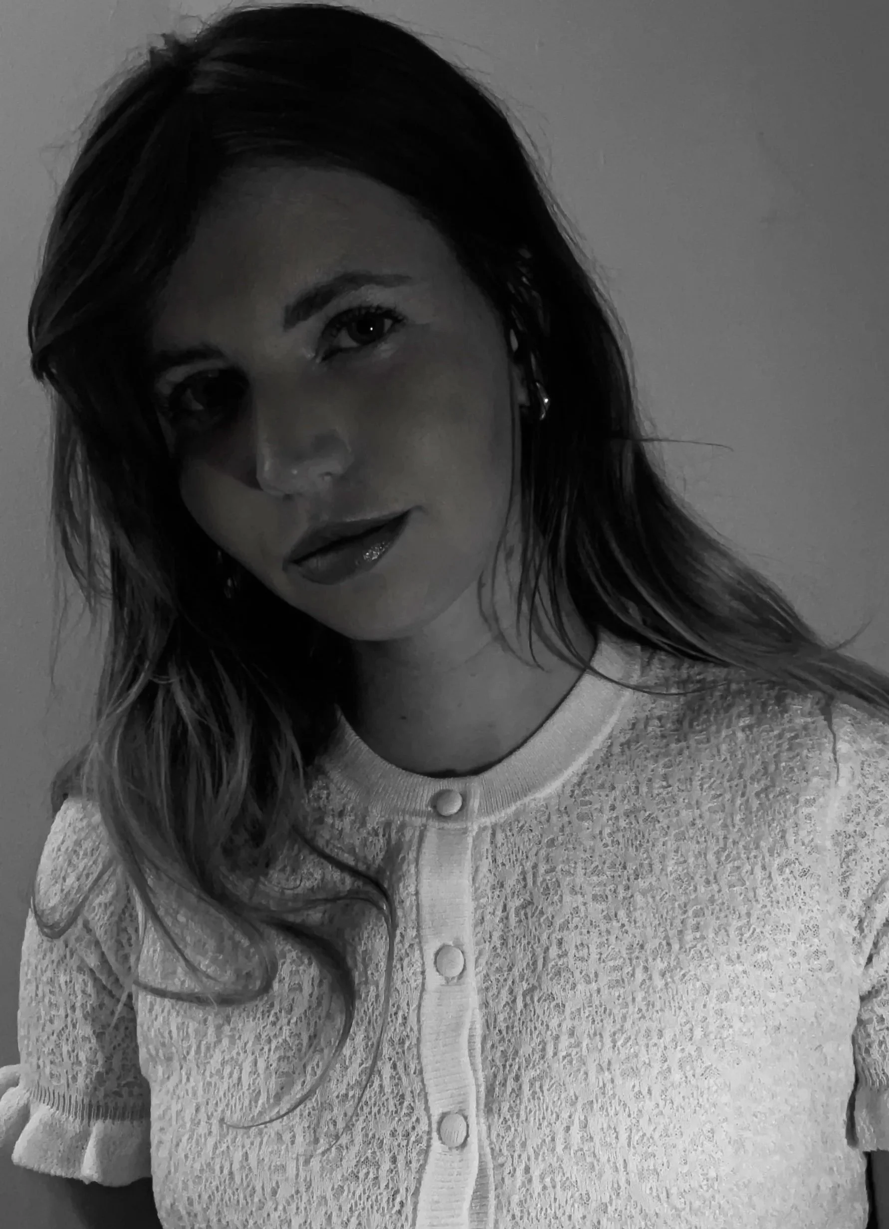 Black and white portrait of a woman with long wavy hair, wearing a textured white cardigan with button details, gazing slightly to the side with a subtle smile.
