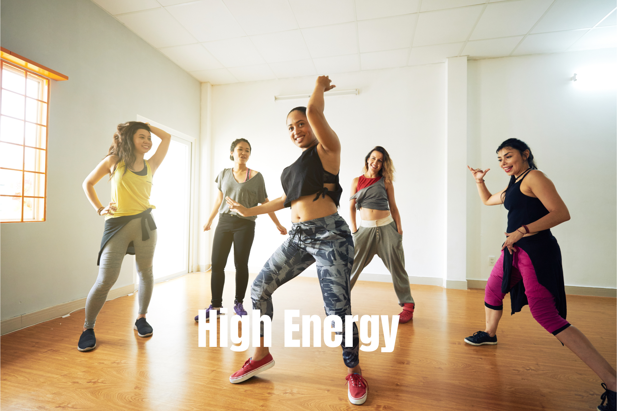 A group of five women dancing energetically in a bright, spacious room with wooden floors and white walls.