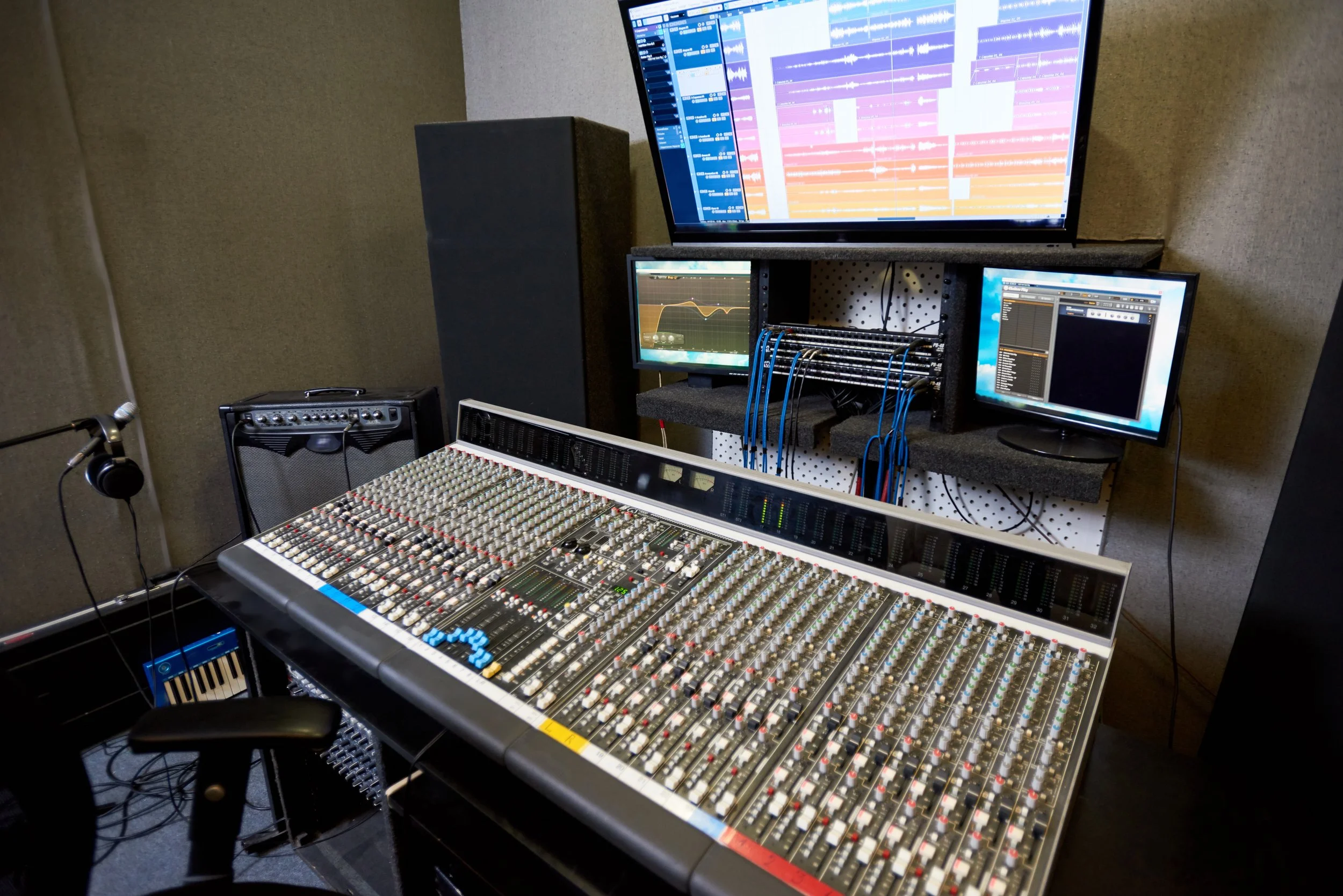 Recording studio with mixing console, headphones, speakers, and two monitors displaying audio editing software