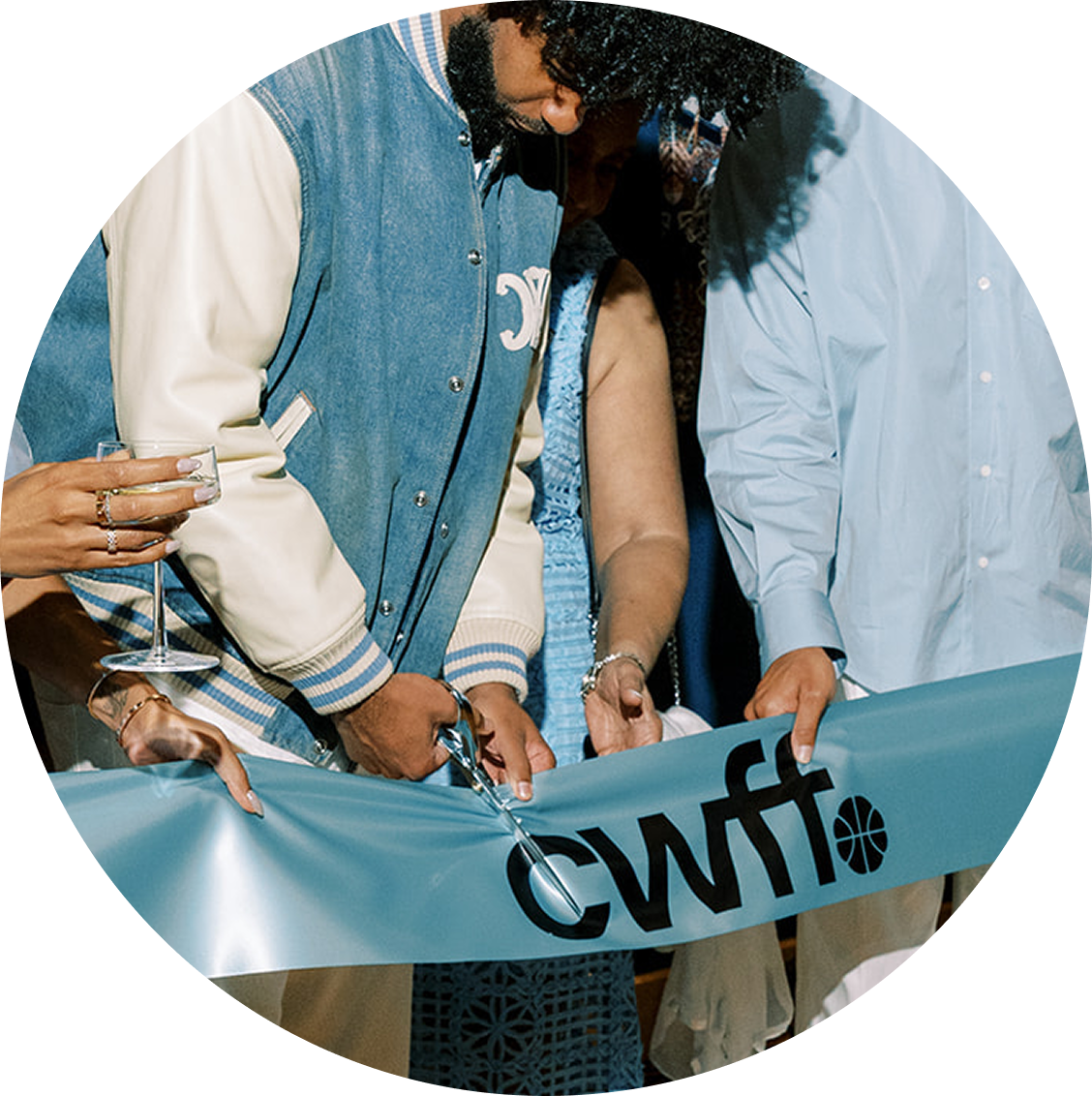 People gathered for a ribbon-cutting ceremony, holding a ribbon with the letters 'CWFT' and a basketball logo, with one person cutting the ribbon.