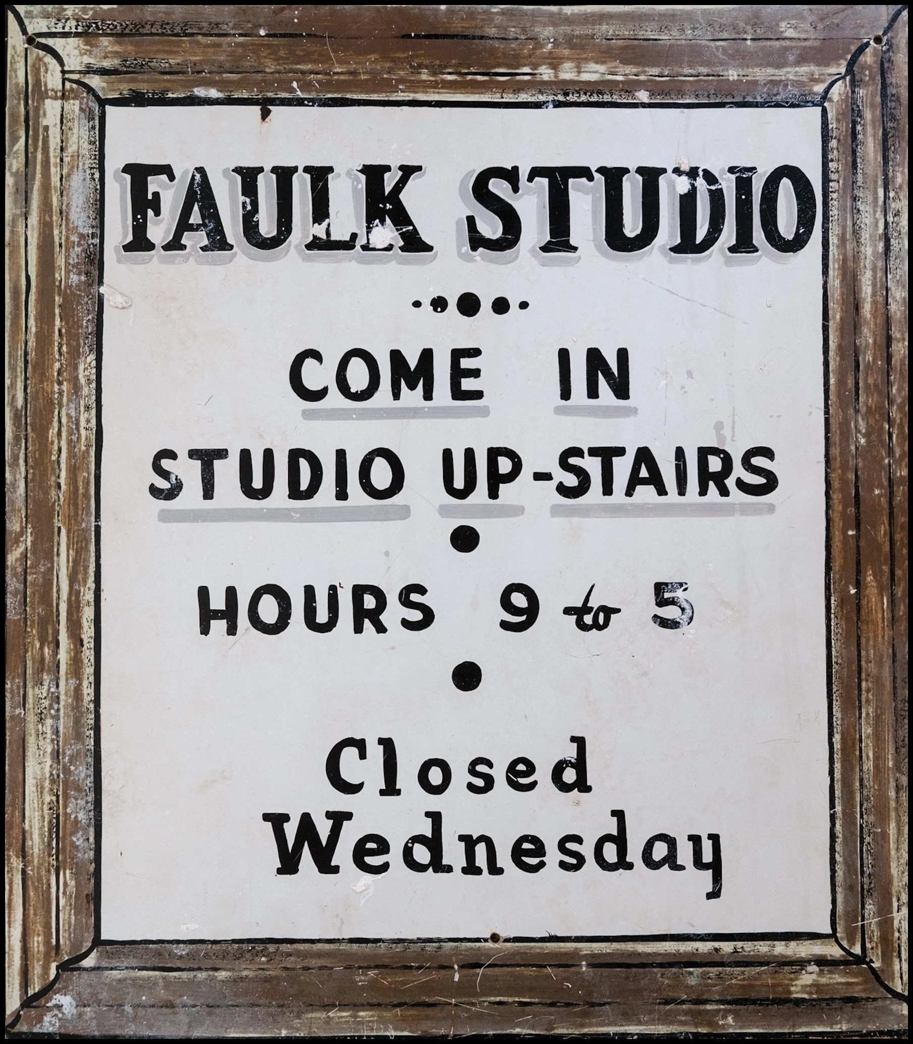 Sign with black border and weathered wood frame that reads 'FALK STUDIO - COME IN, STUDIO UPSTAIRS - CLOSED WEDNESDAY' in black capital letters on a white background.