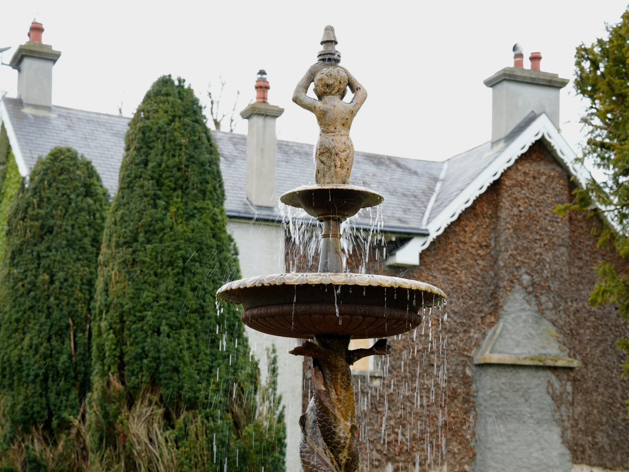 Stone fountain in front of a restored 1500s manor house with ivy-covered exterior and traditional detailing.