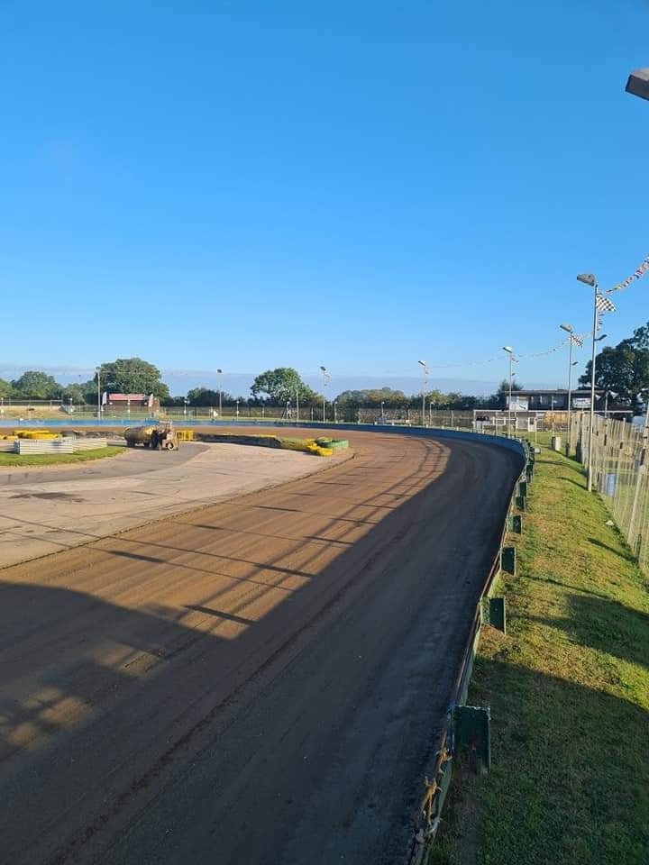 Empty Northampton Shaleway track, surrounded by a fence, with a few yellow barriers on the track, under a clear blue sky.