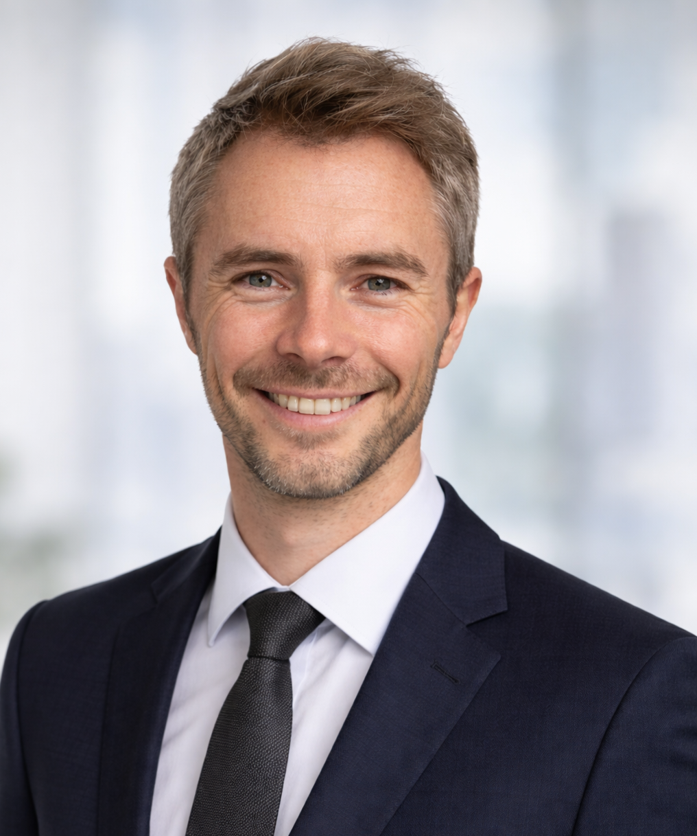 Portrait d'un homme en costume, souriant, dans un environnement professionnel.