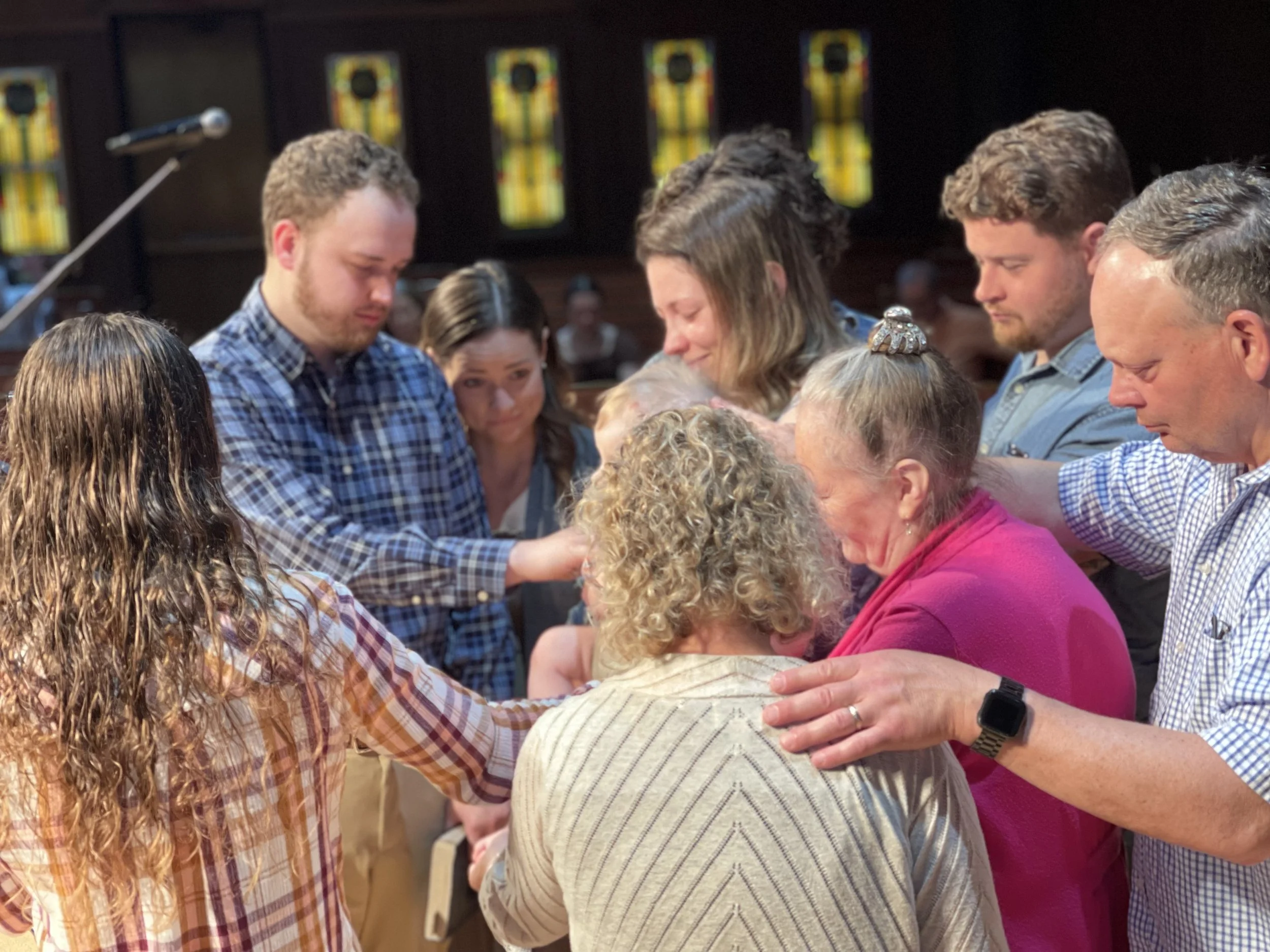 A group of people praying together with their heads bowed and hands placed on each other's shoulders.