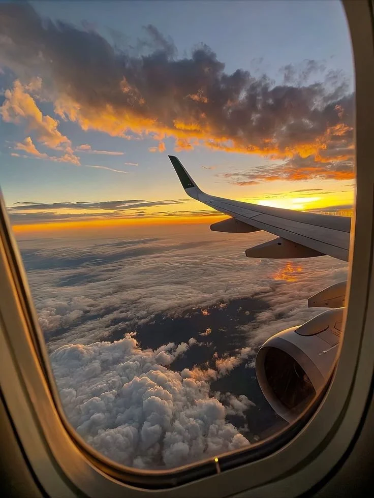 View of a sunset from an airplane window, with clouds below and the plane's wing visible.