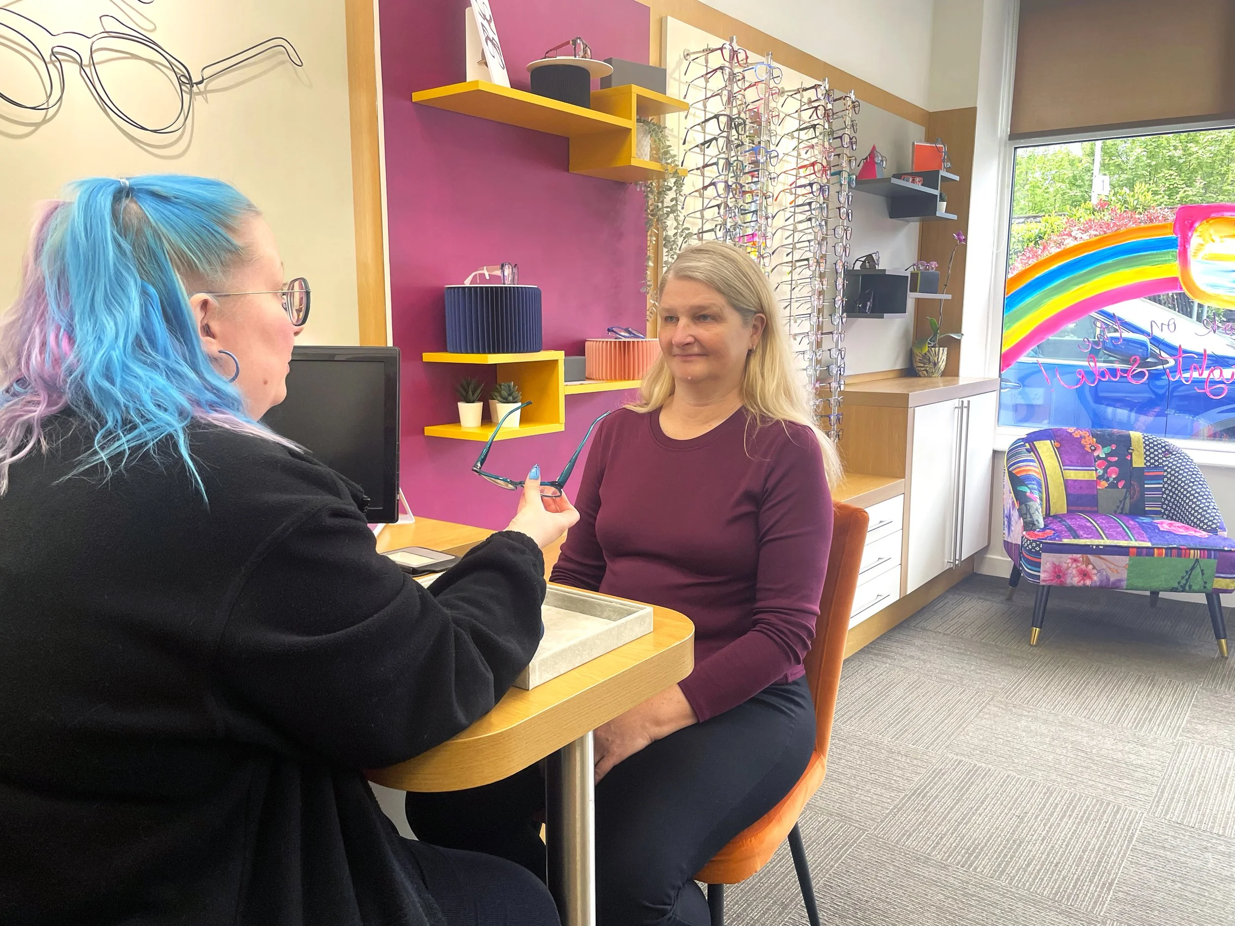 A colleague is advising and helping a customer try on different frames in store.