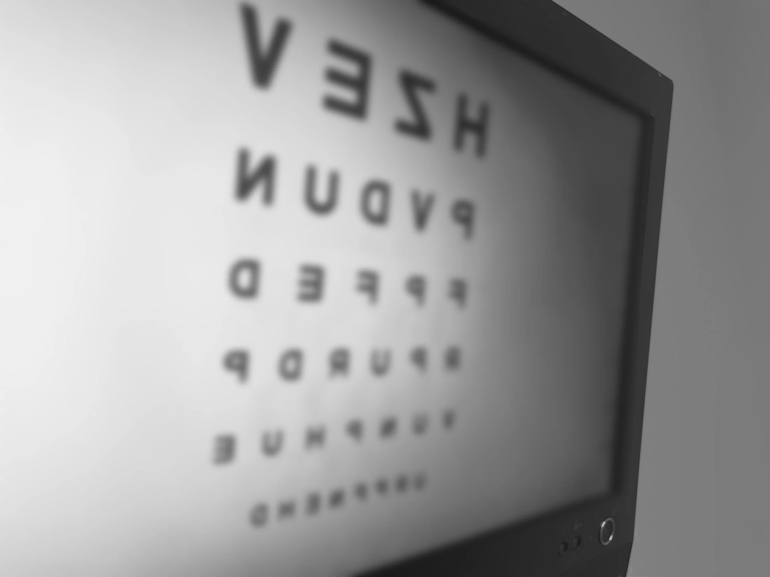 Close-up of a Snellen eye chart on a white background, with blurry black letters, used for vision testing.