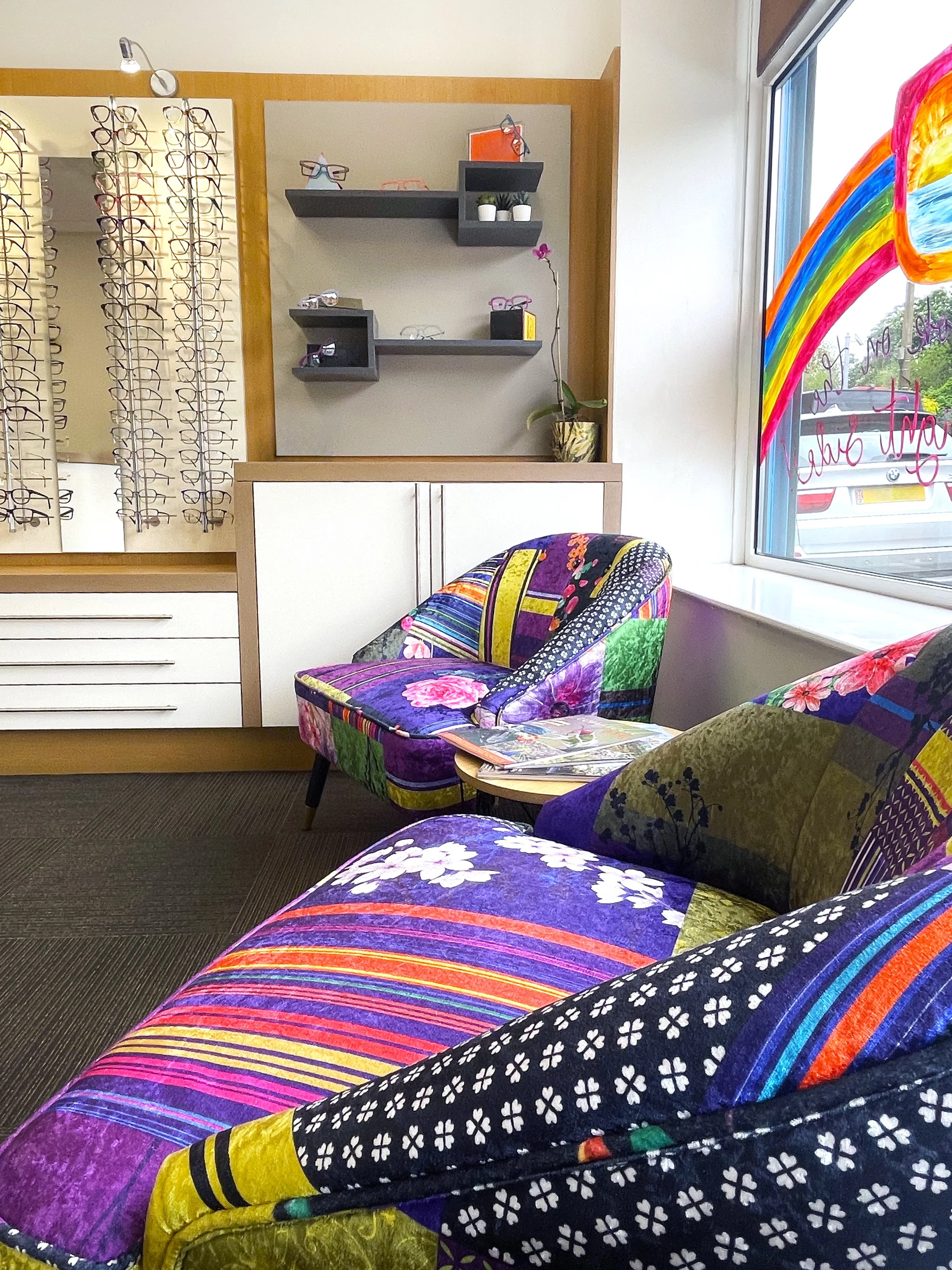 Colorful patchwork armchair with floral and striped patterns in front of a window with rainbow-coloured window art inside the main reception.
