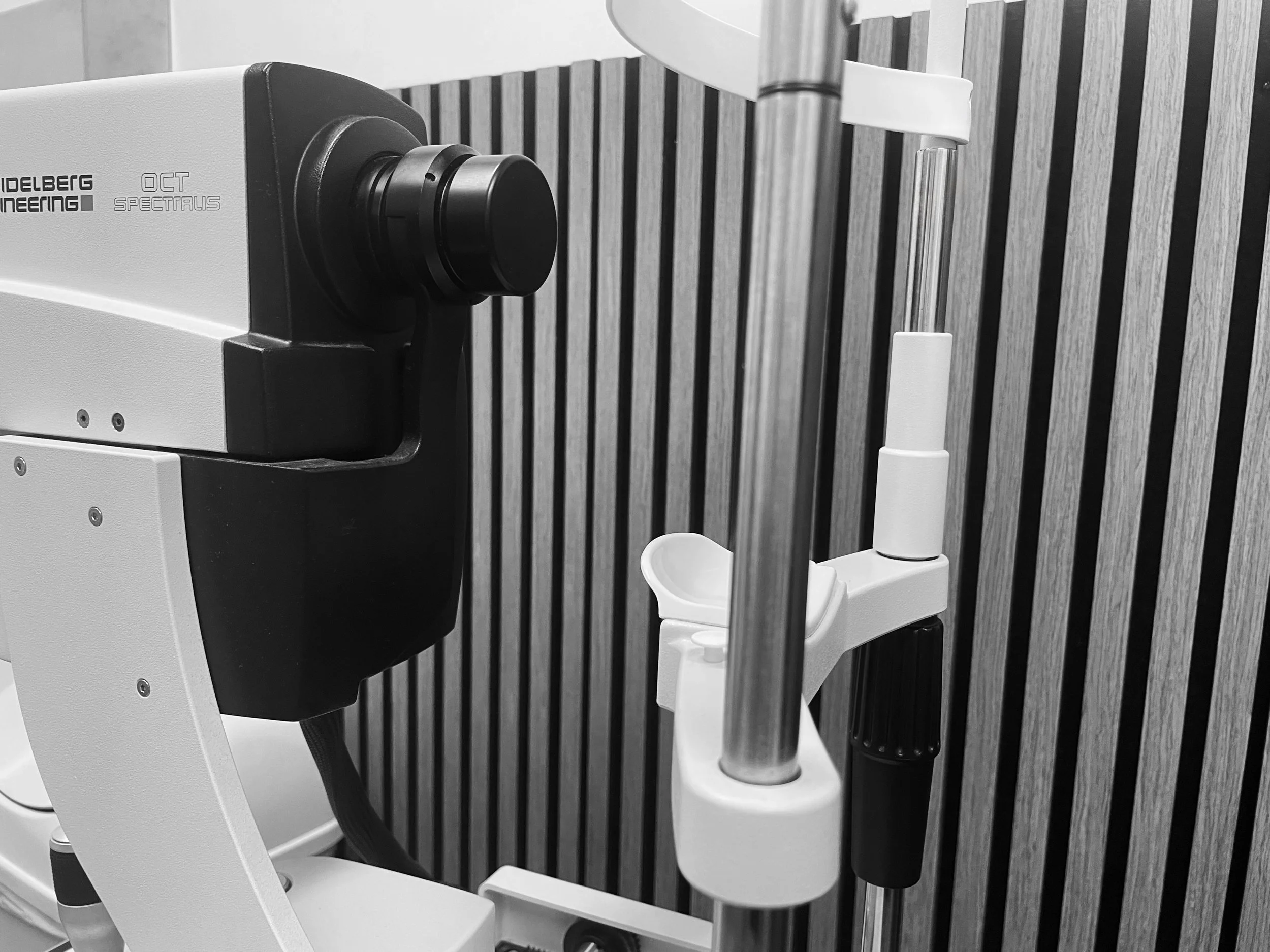 Close-up of a optometrist instrument with a black and white body, a large black circular component, and a vertical metallic component, set against a background of vertical wooden slats.