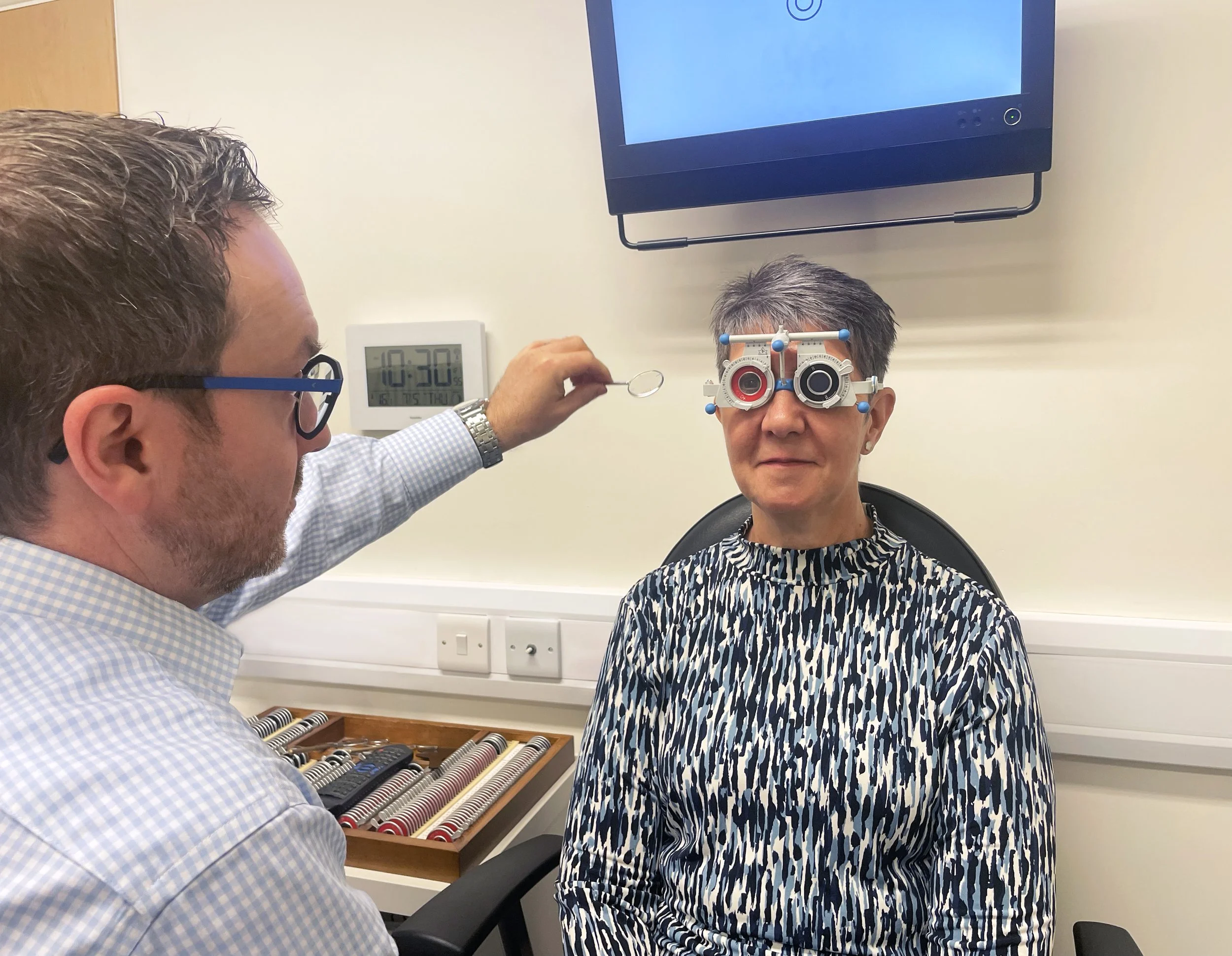 Mark Holloway examining a patient's eyes with a trial frame device at the practice.