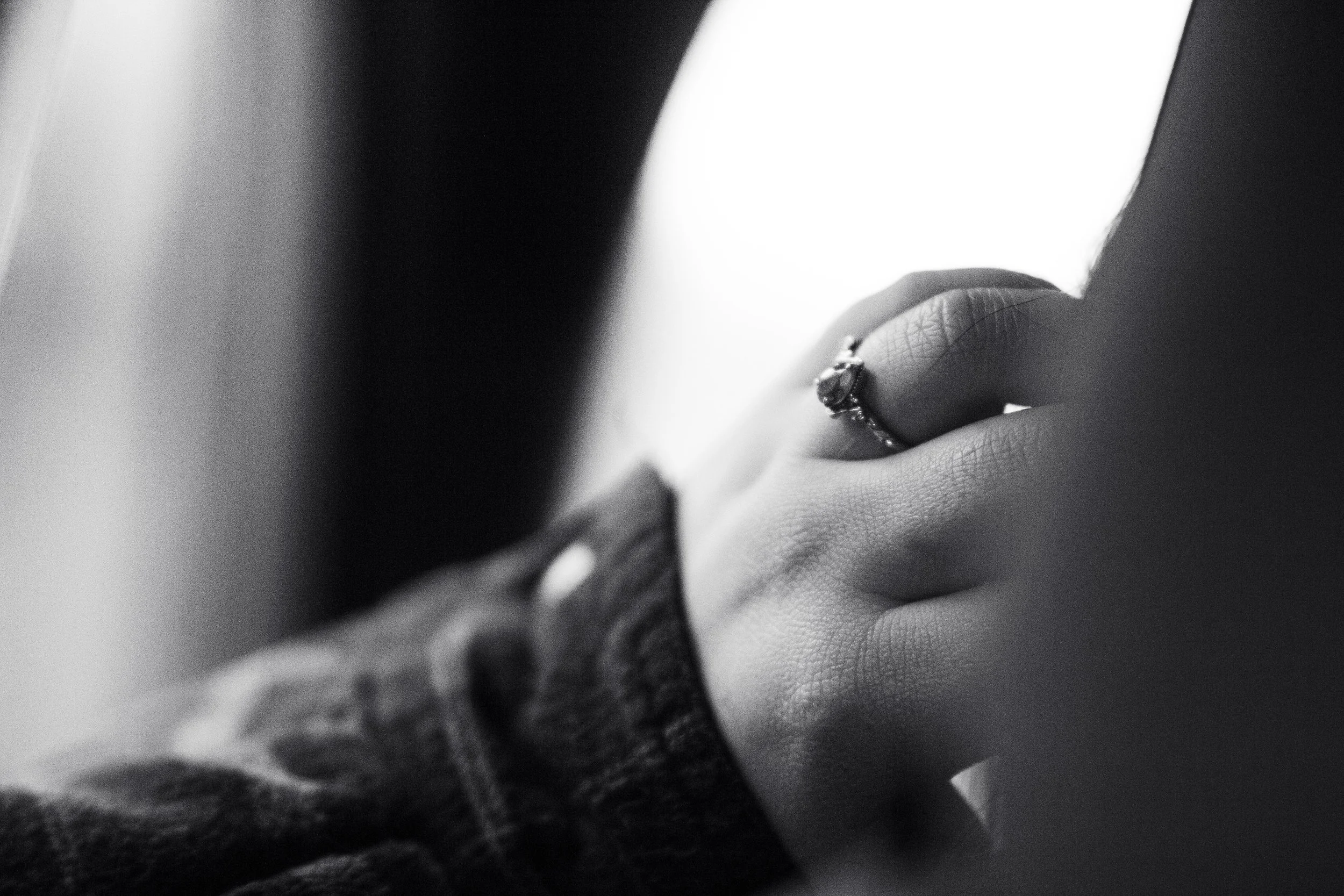 Close-up of a person's hand resting on their face, wearing a ring on their finger, in black and white.