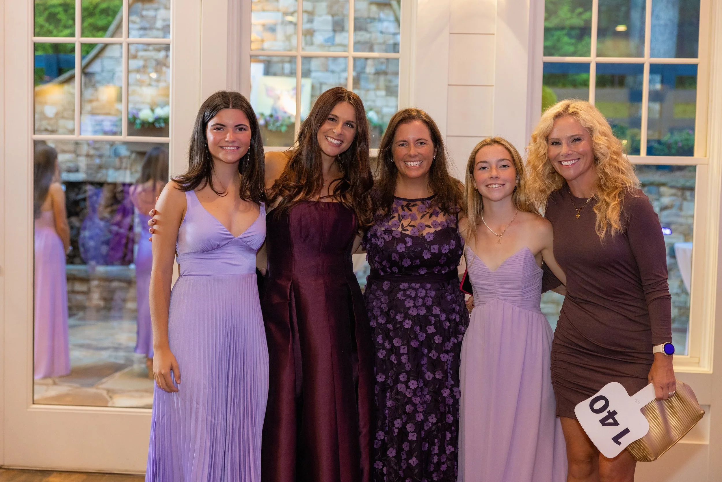Group of five women posing and smiling in front of glass doors during a celebration or event.
