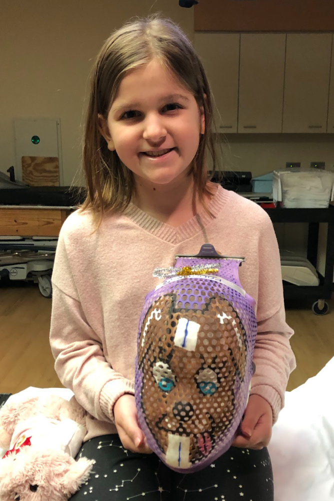 Young girl smiling and holding a decorated plush backpack with a dog face design.