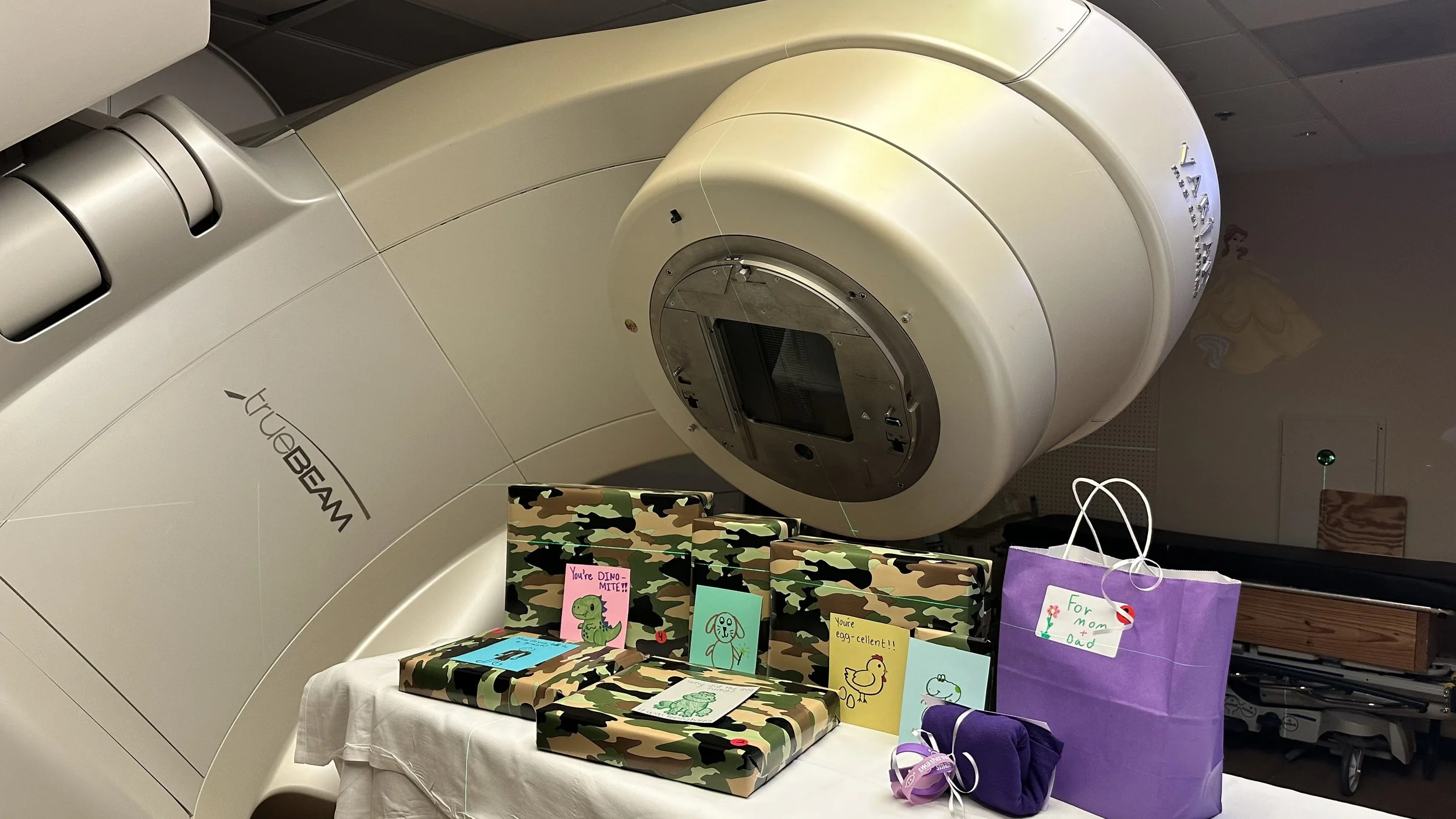 A large medical imaging machine, likely an MRI or CT scanner, with a display screen and several colorful cards and gift bags with children's drawings and messages placed in front of it.