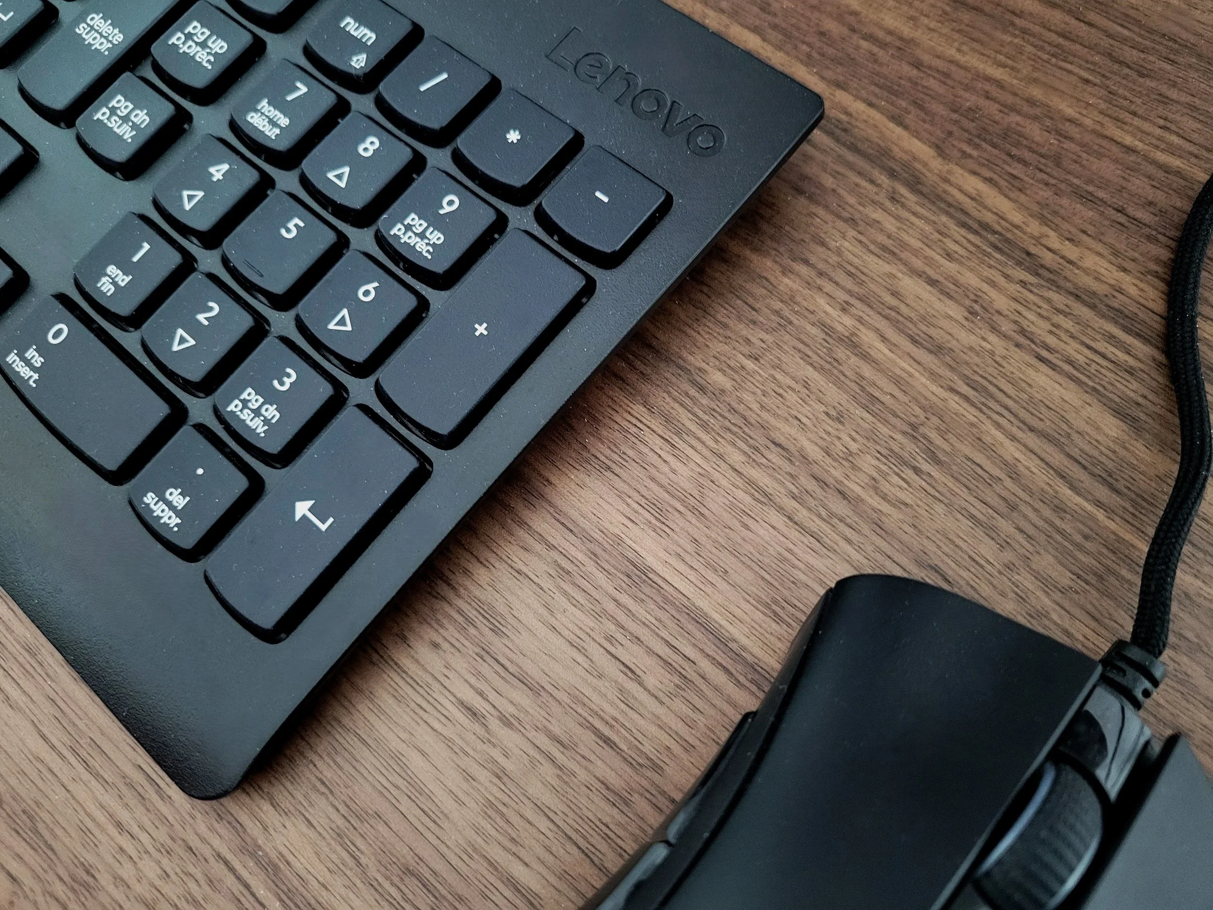 Close-up of a black Lenovo computer keyboard on a wooden desk, with a wired computer mouse to the bottom right.