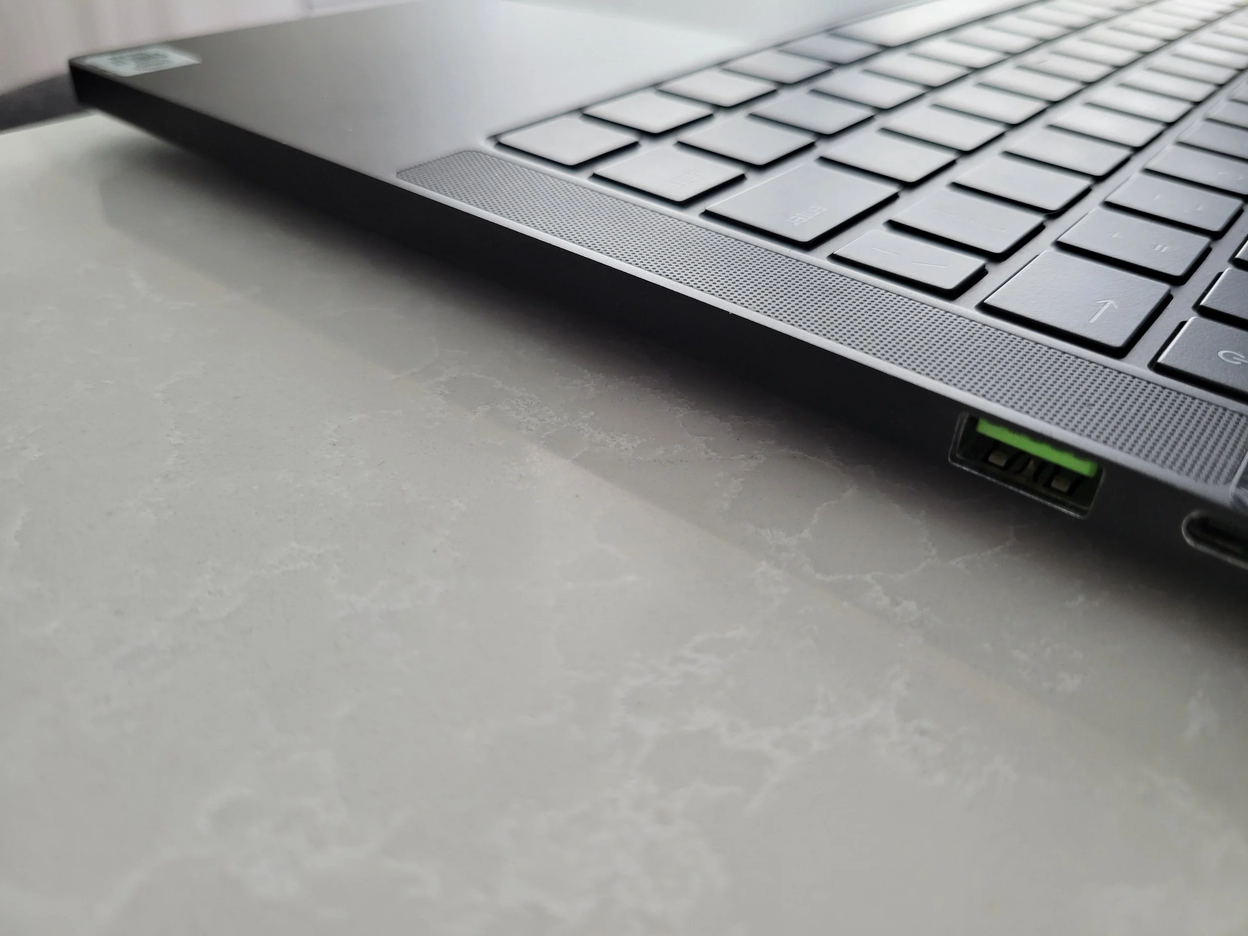Close-up of the corner of a silver laptop with a black keyboard, resting on a light-colored textured surface.
