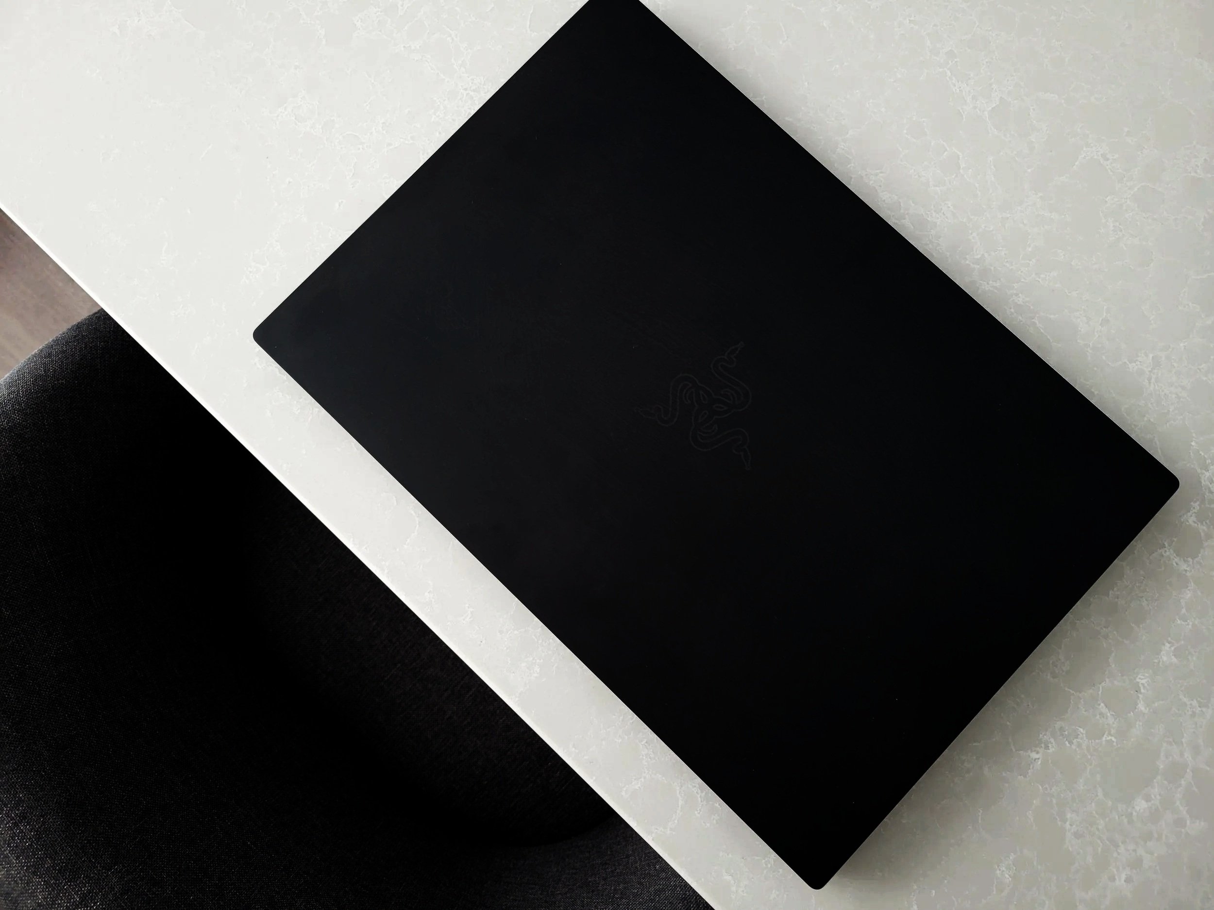 A black laptop with a Razer logo on the lid, placed on a white textured table.