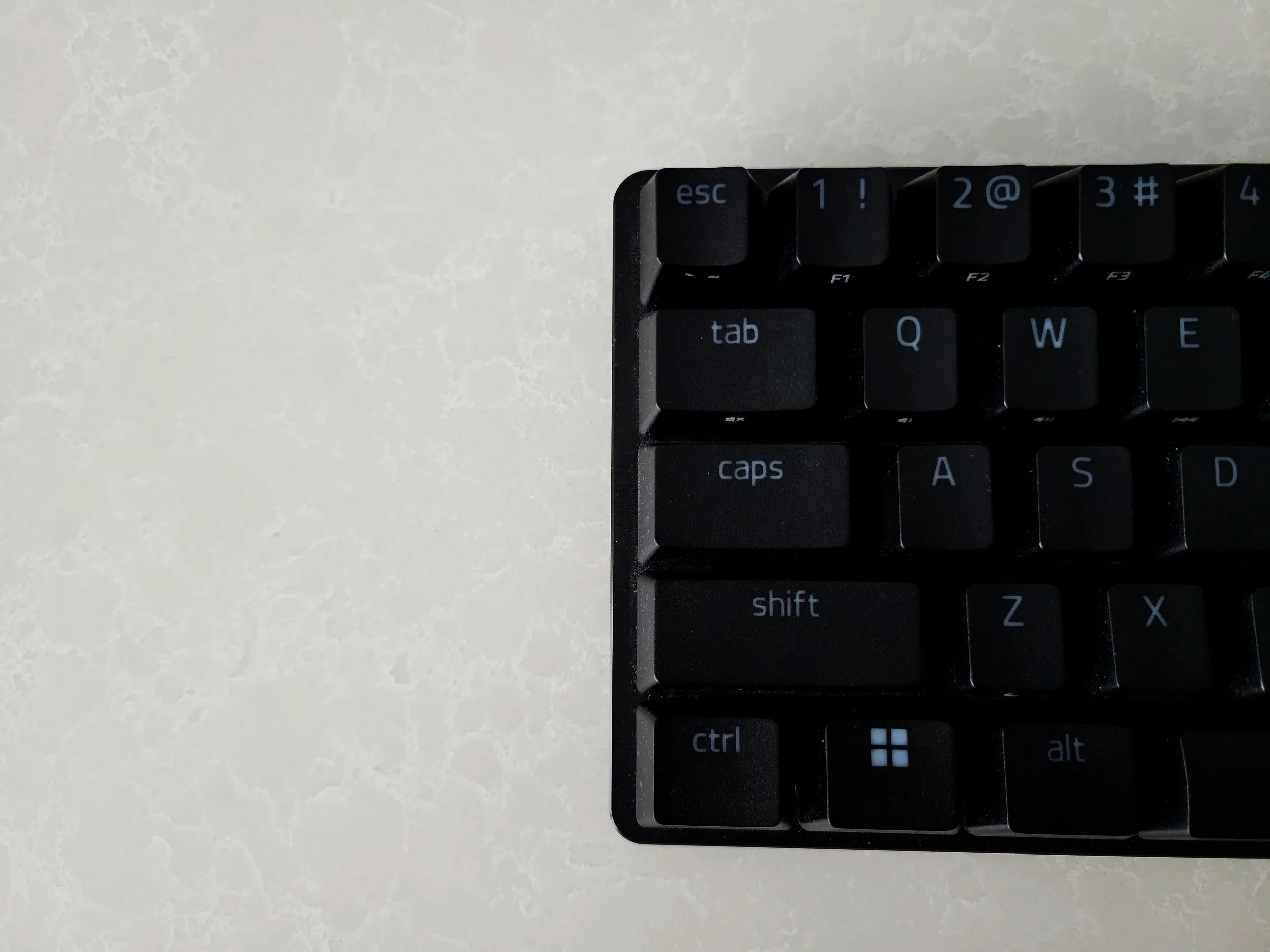Partial view of a black computer keyboard on a white textured surface, showing keys including escape, tab, caps lock, shift, control, Windows, and alt.