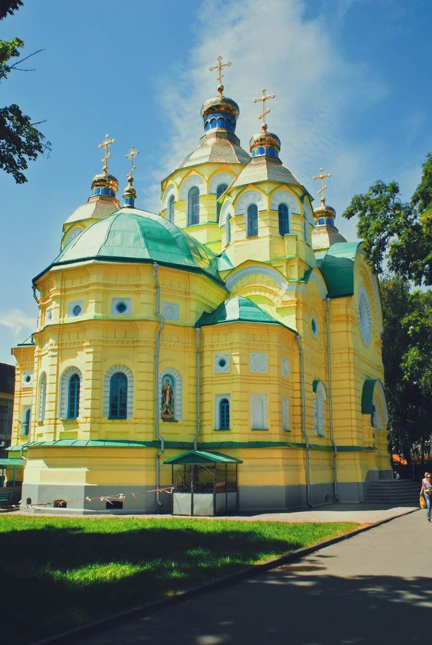 A yellow Orthodox church with multiple domes topped with crosses, set against a blue sky with some clouds.
