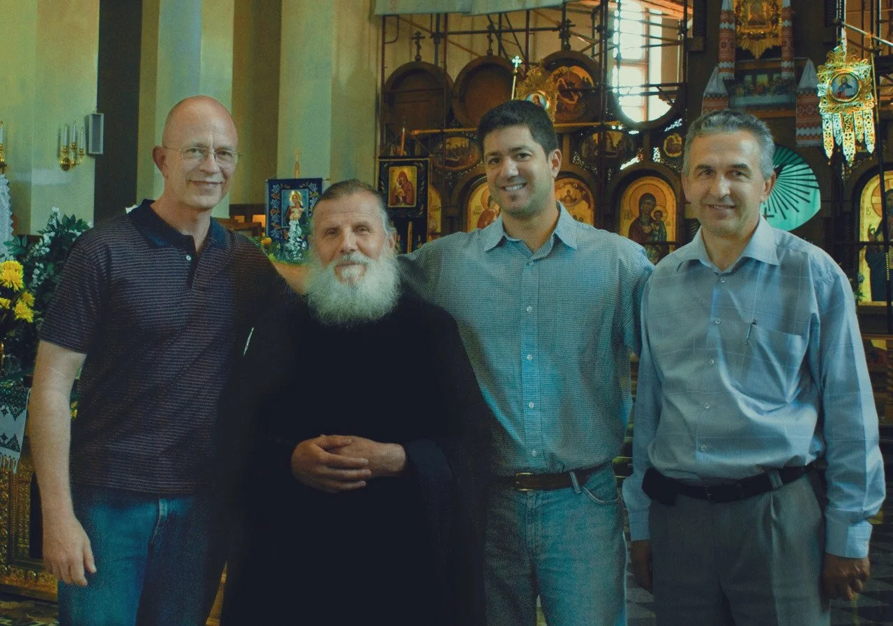 Four men standing together in a church with religious icons and decorations in the background.