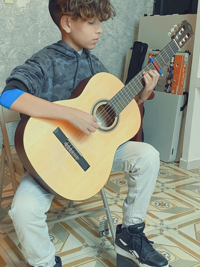 A young boy sitting on a chair playing an acoustic guitar.