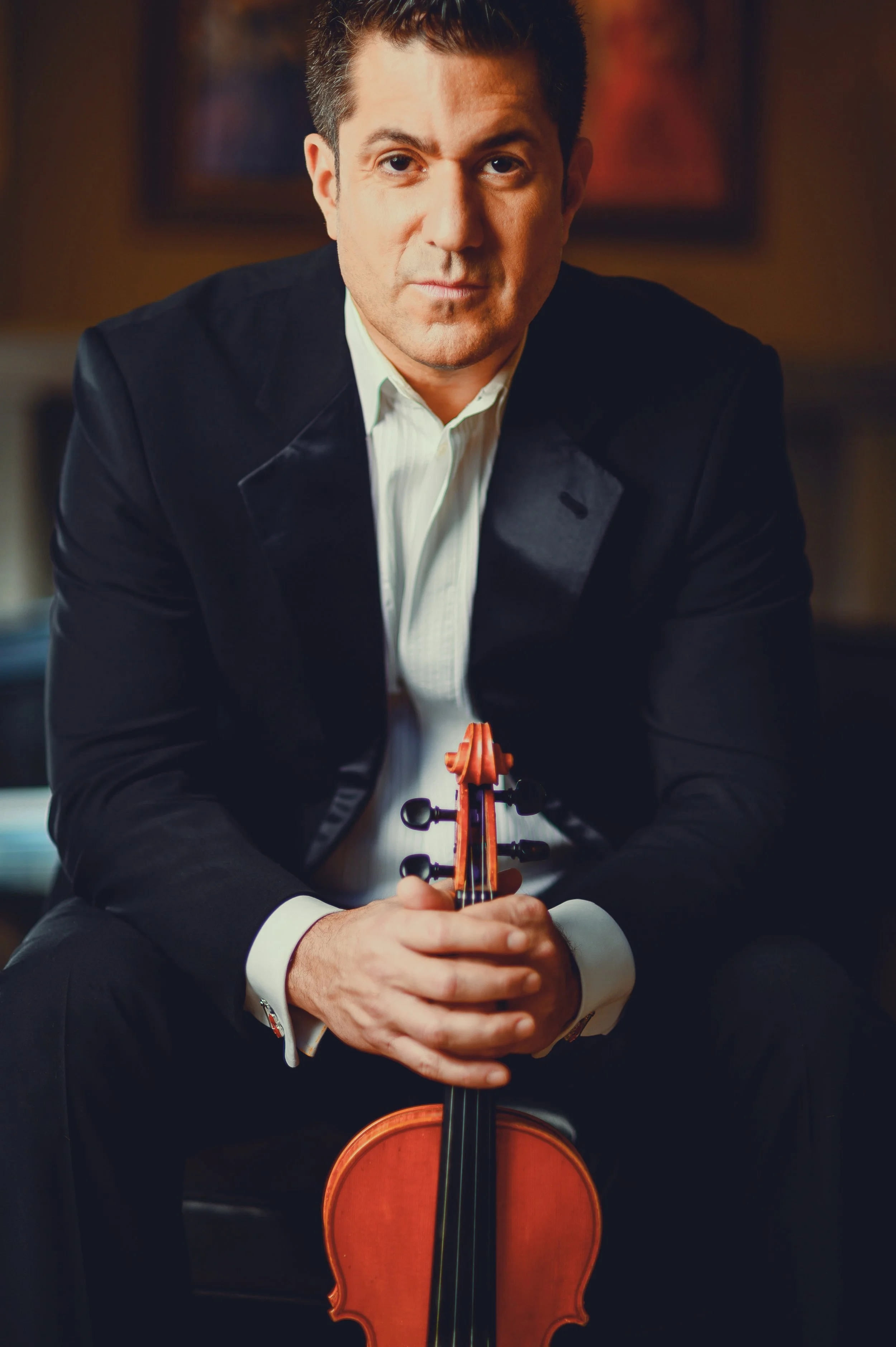 A man in a tuxedo holding a violin in a formal setting.