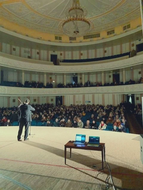 A performer on stage in a large, ornate theater with an audience watching.