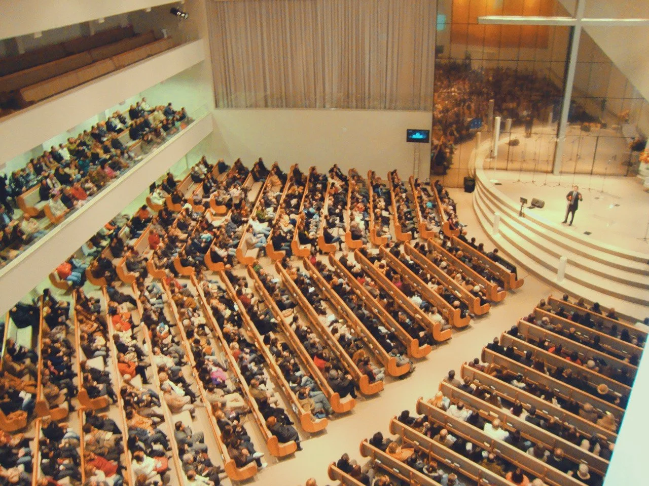 Large congregation seated in an auditorium with a speaker on stage.