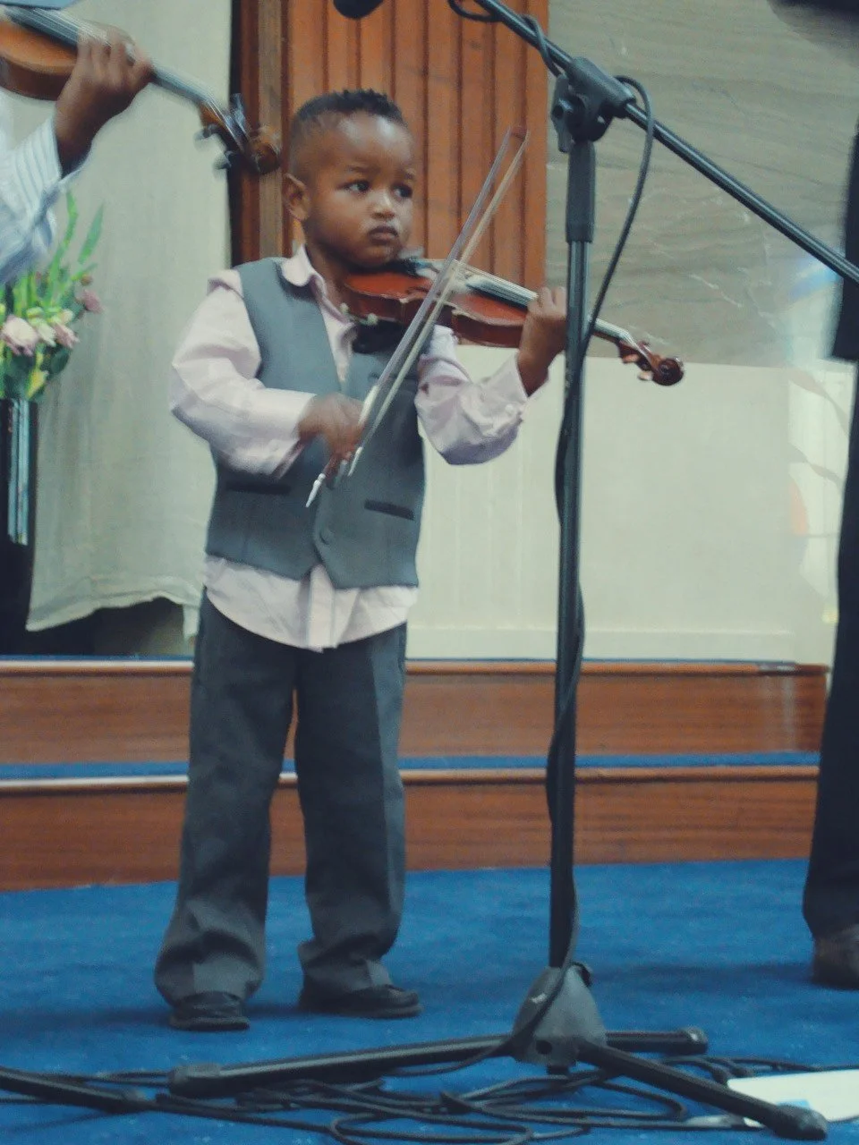 Young boy playing the violin on stage during a performance with a microphone in front of him.
