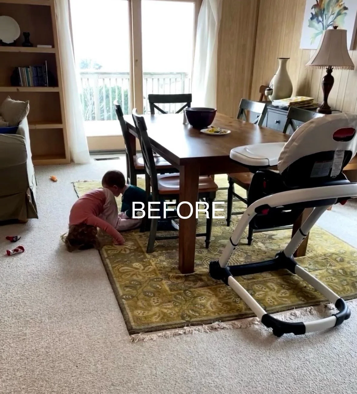 before photo: Living room with a dining table, two children playing on a yellow patterned rug, high chair, sliding glass door leading to a balcony, bookshelf, and decorative vases and lamp on side tables.