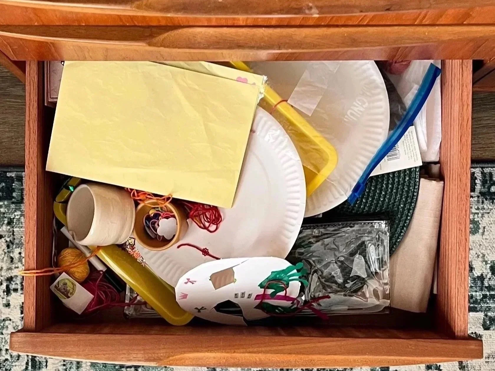 Open wooden drawer containing party supplies, including paper plates, cups, napkins, balloons, and assorted decorations.
