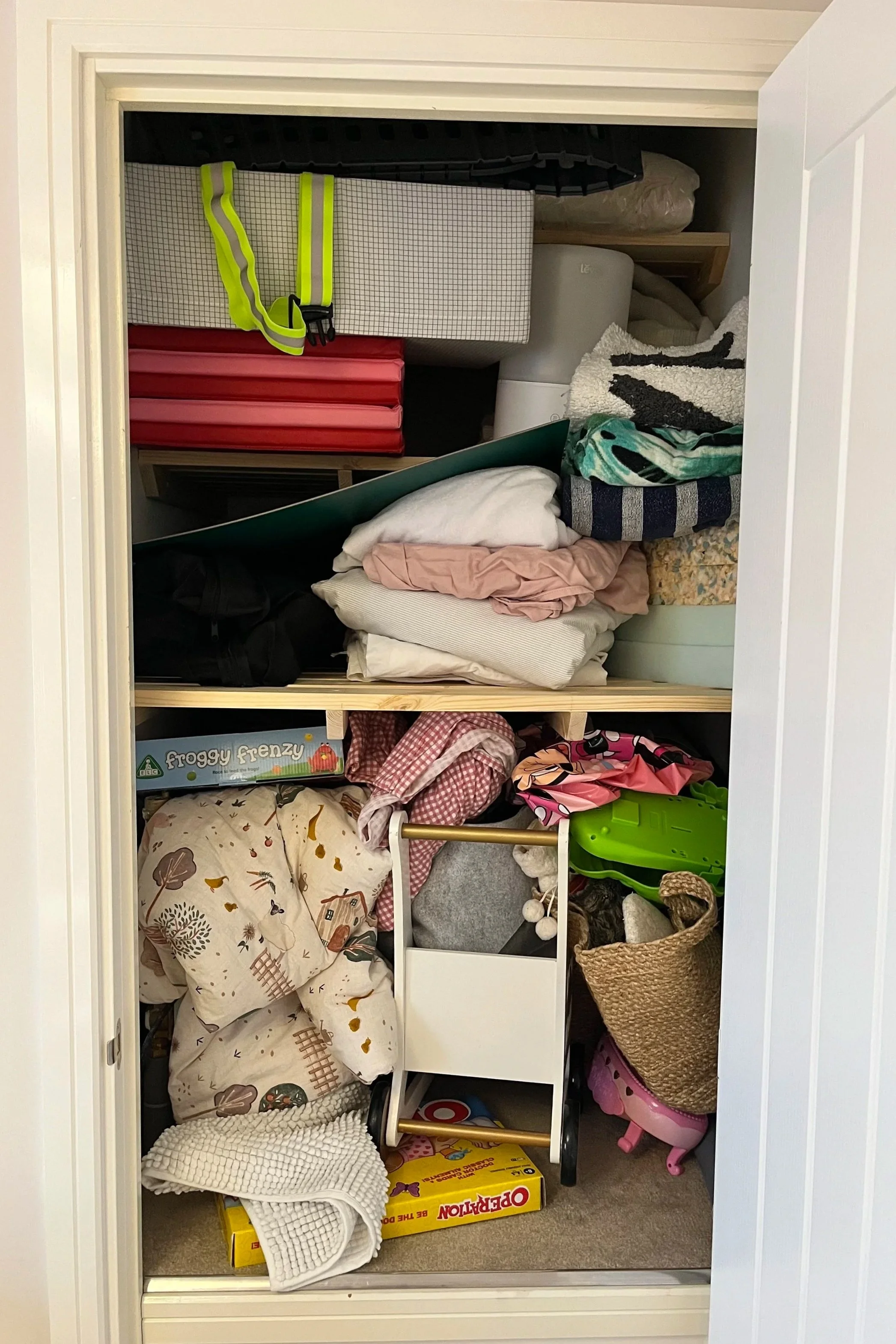A cluttered closet with various folded clothes, blankets, and toys stacked on shelves and the floor.