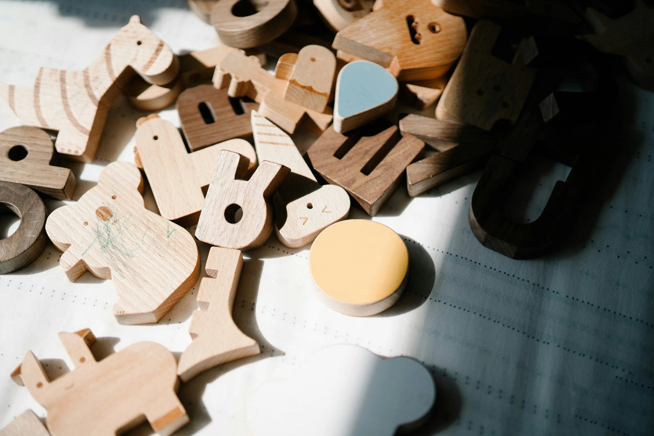 A collection of wooden and plastic alphabet and number blocks scattered on a surface, with some blocks showing letters and numbers and others featuring shapes like hearts and circles.