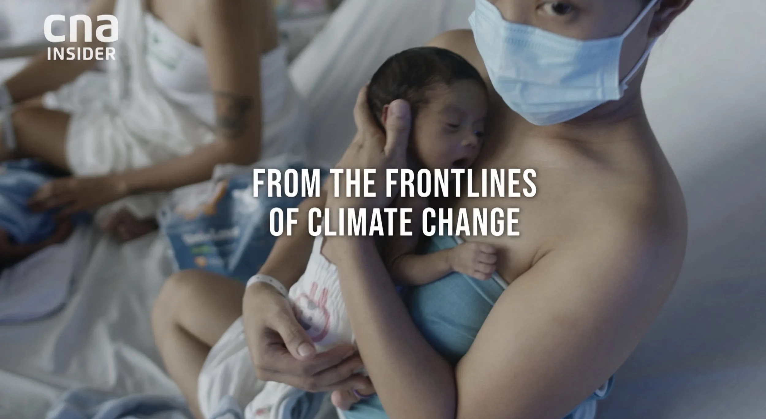 A shirtless person wearing a face mask holds a newborn baby close to their chest in a hospital setting, with medical staff and another patient visible in the background. The overlay text says, 'From the frontlines of climate change.'