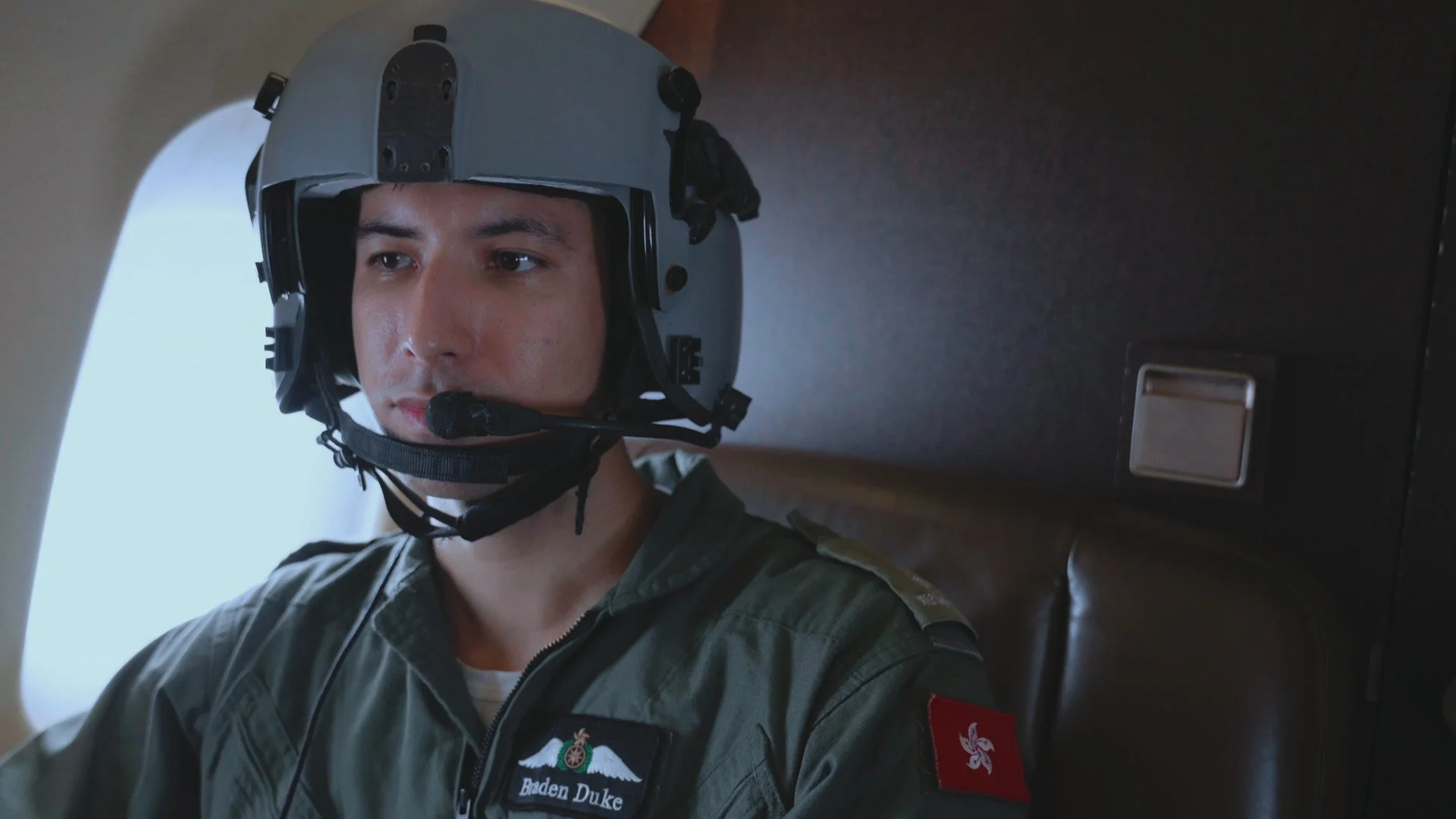 A man in military uniform wearing a helmet with a microphone, sitting inside a vehicle or aircraft.