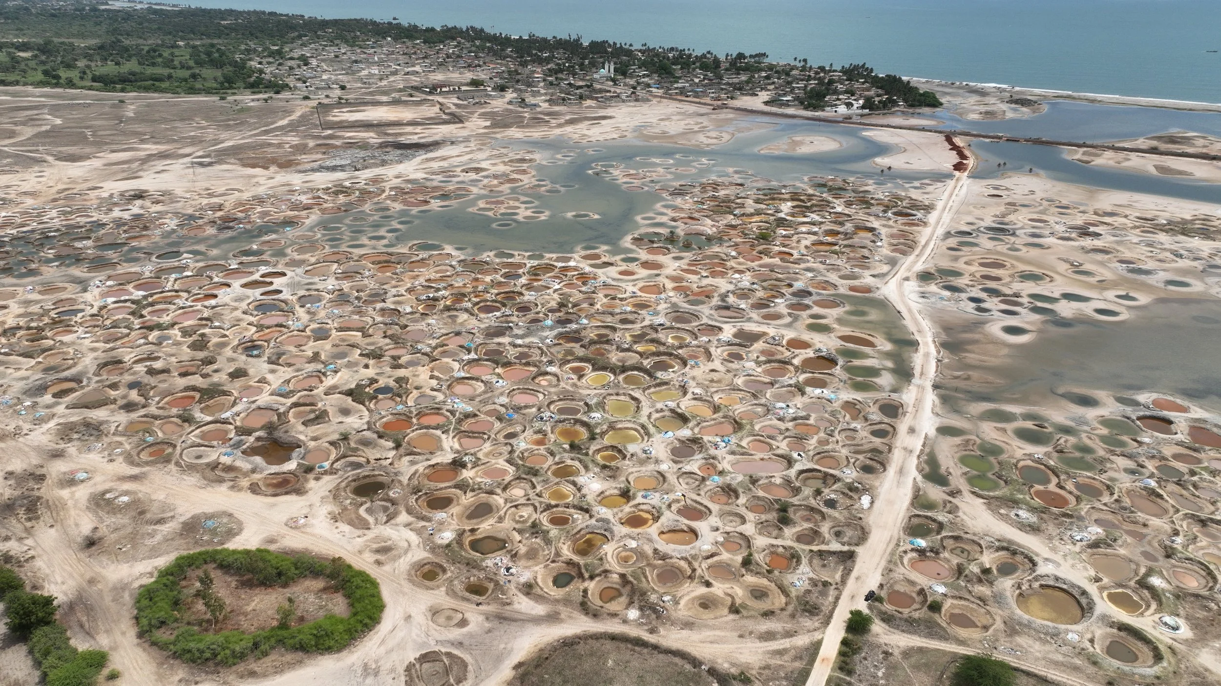 Aerial view of a salt evaporation pond with many circular ponds of various colors in a rural area near the coast.