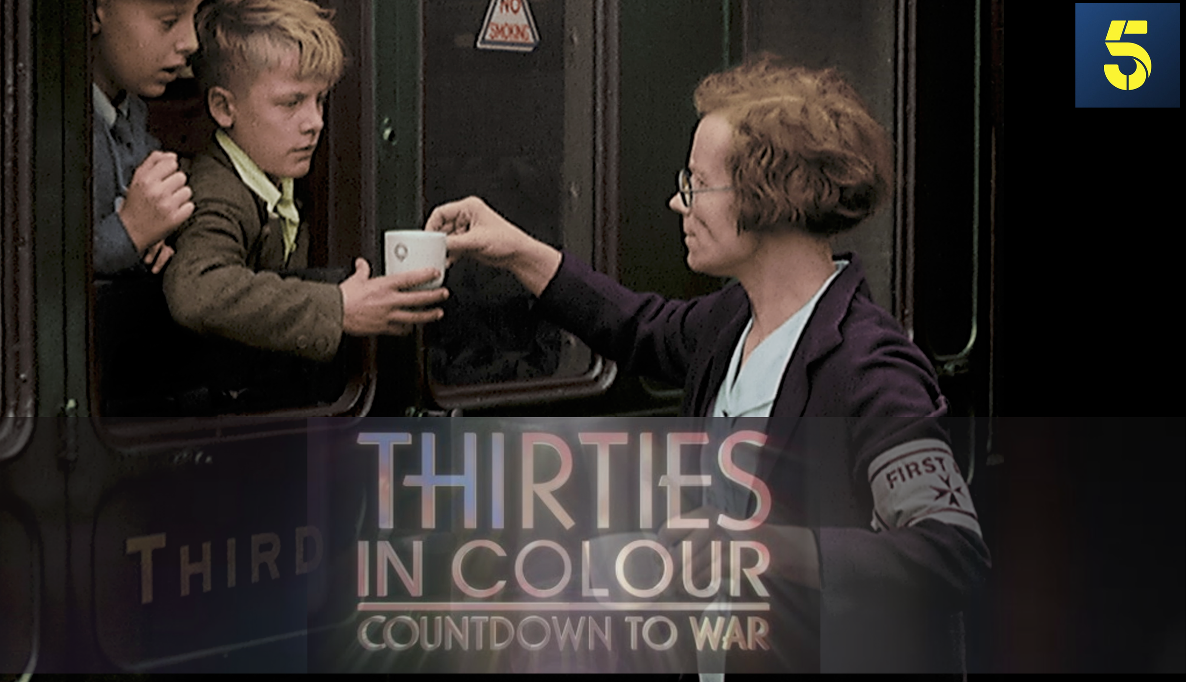 A woman with short reddish hair and glasses handing a coffee cup to a young boy on a train. Two other children are behind the boy, looking on. The train window has a sign that says 'NO SMOKING'. Part of a colorful sign with the words 'THIRD IN COLOR' is visible at the bottom.
