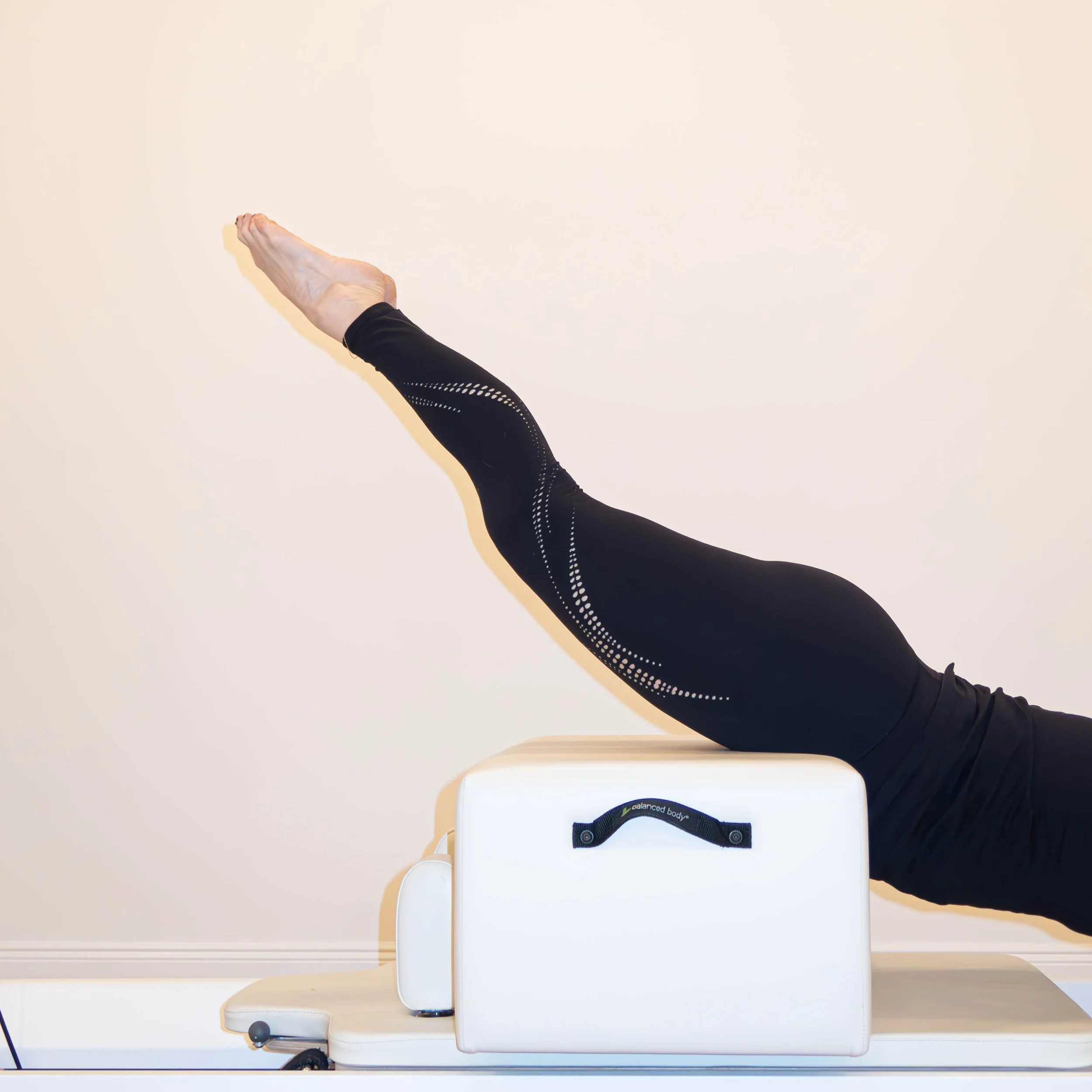 Person performing Pilates exercise using Reformer machine, focusing on stretched arm and extended leg