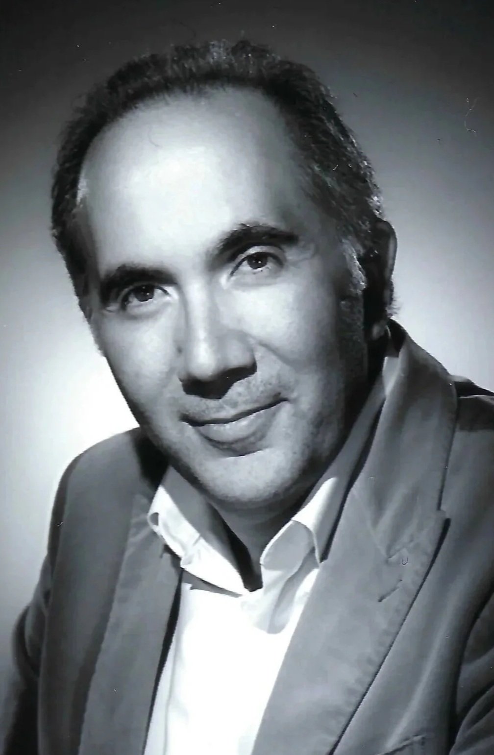 Black and white portrait of a man in a suit, smiling slightly, with short dark hair.