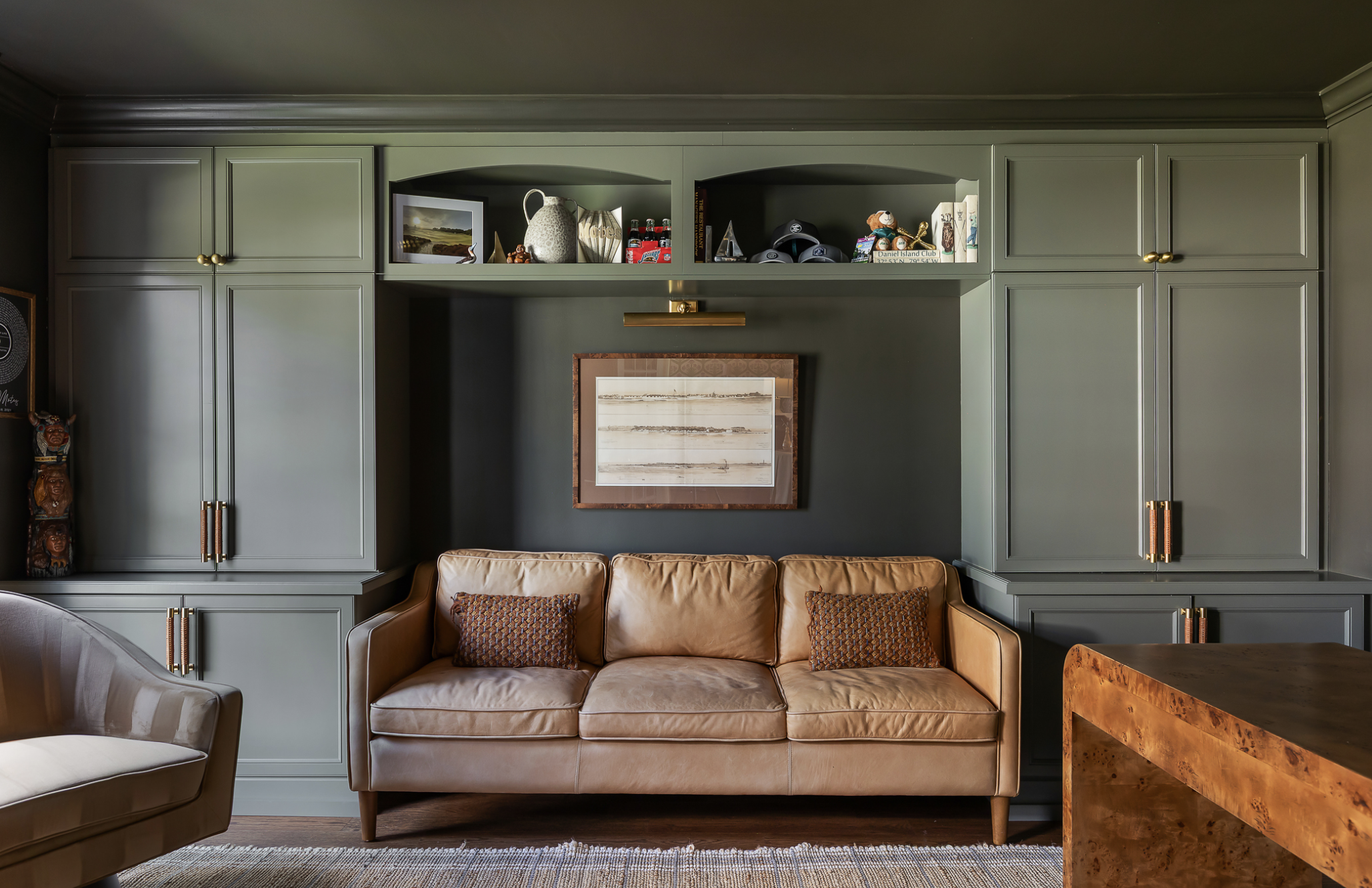 Living room with a tan leather sofa, green built-in cabinets, a framed artwork on the wall, and decorative objects on the shelves.
